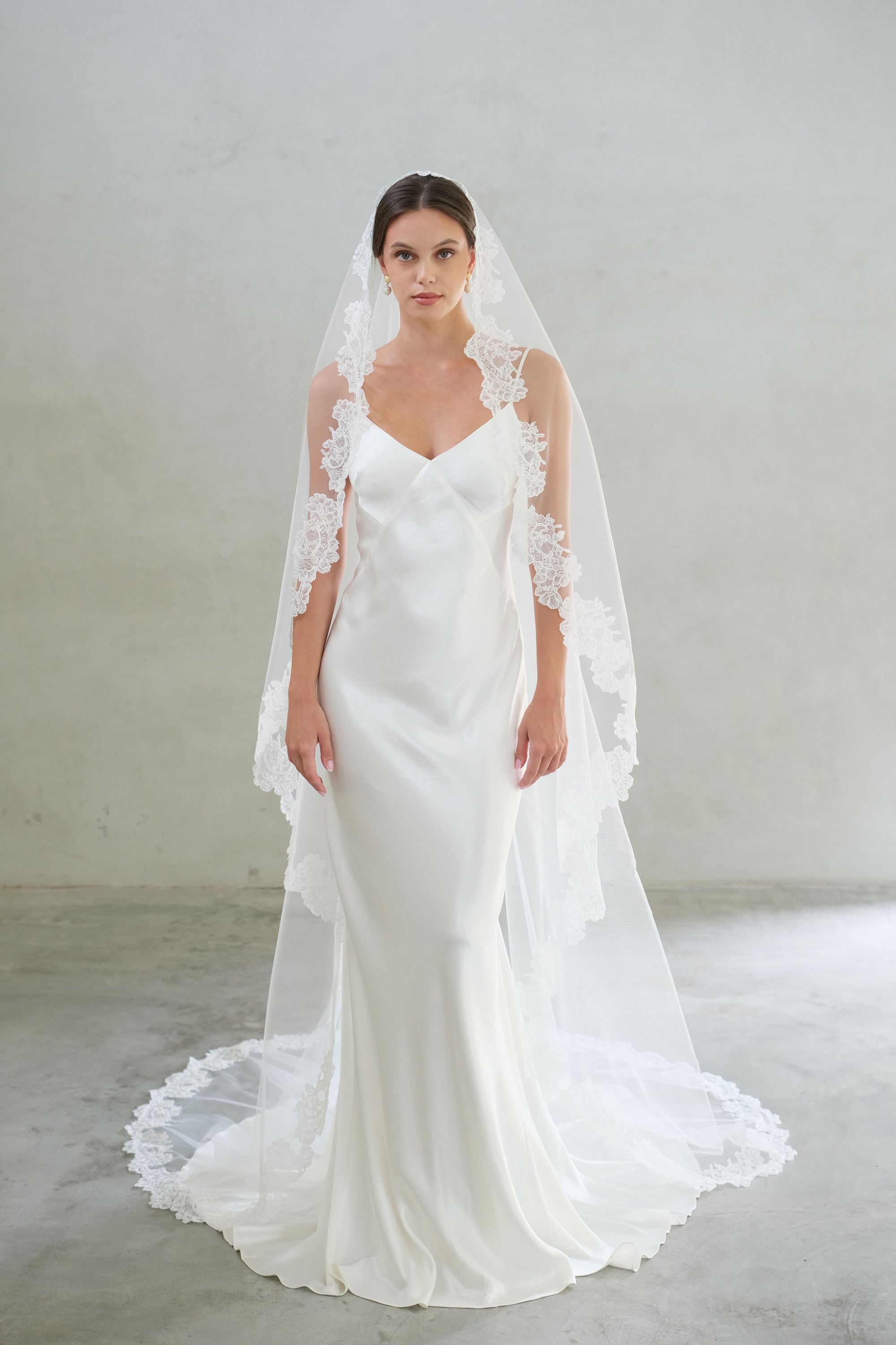 Full length front facing bride wears lace trimmed mantilla style wedding veil