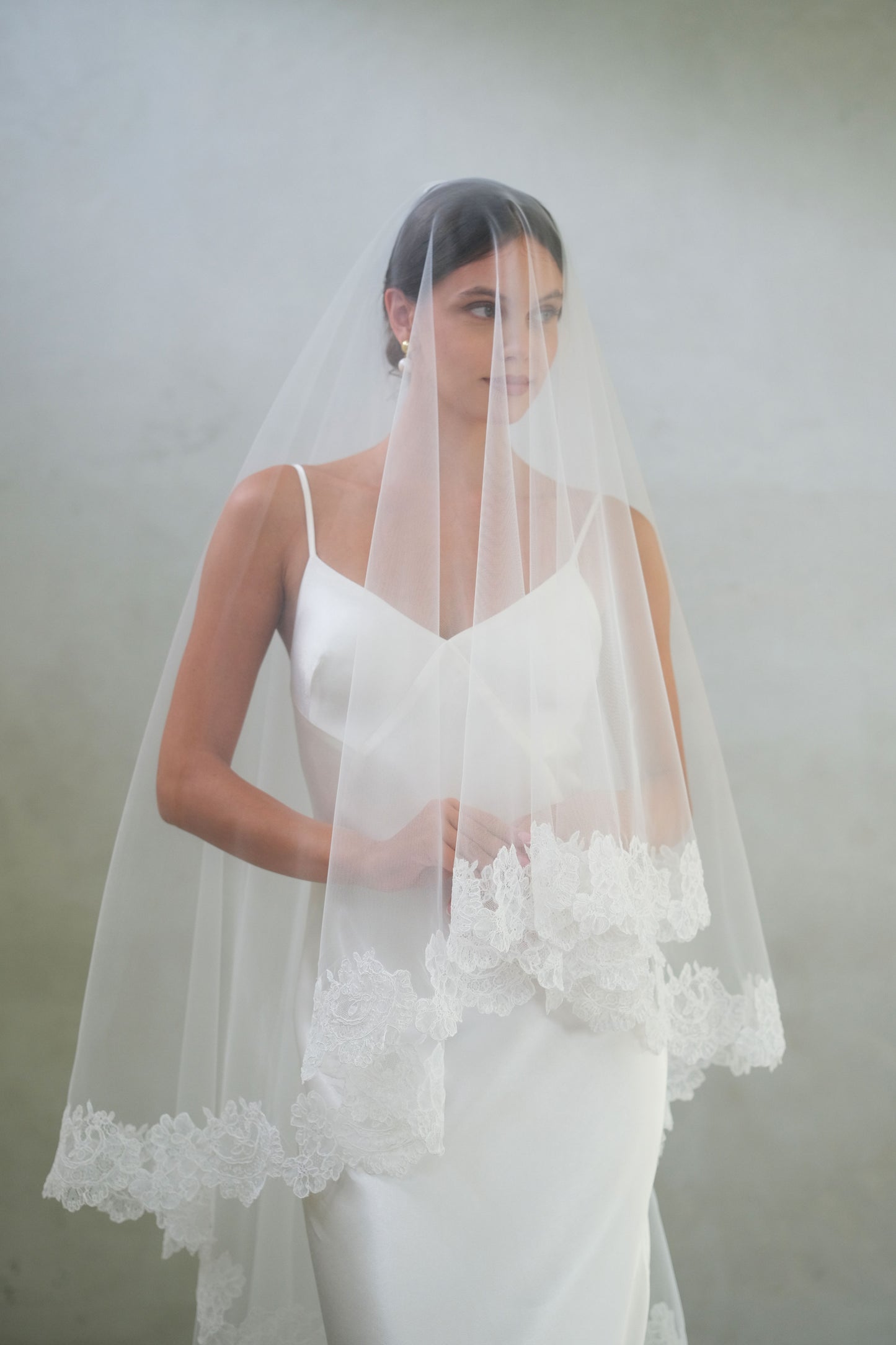 Half length, front facing bride wears lace trimmed wedding veil showing blusher down