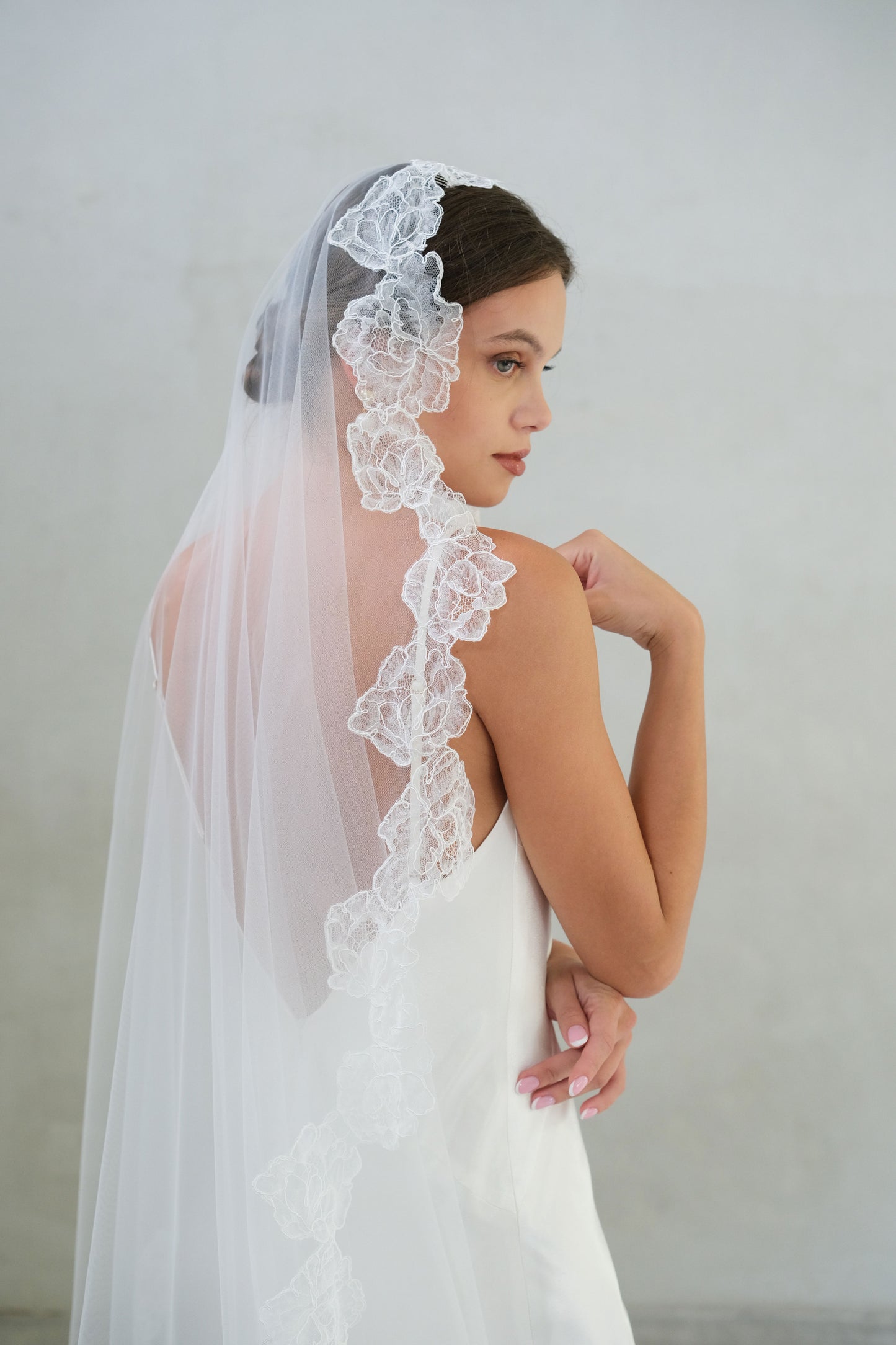Half-length profile view of bride wearing floral lace-edged mantilla-style veil