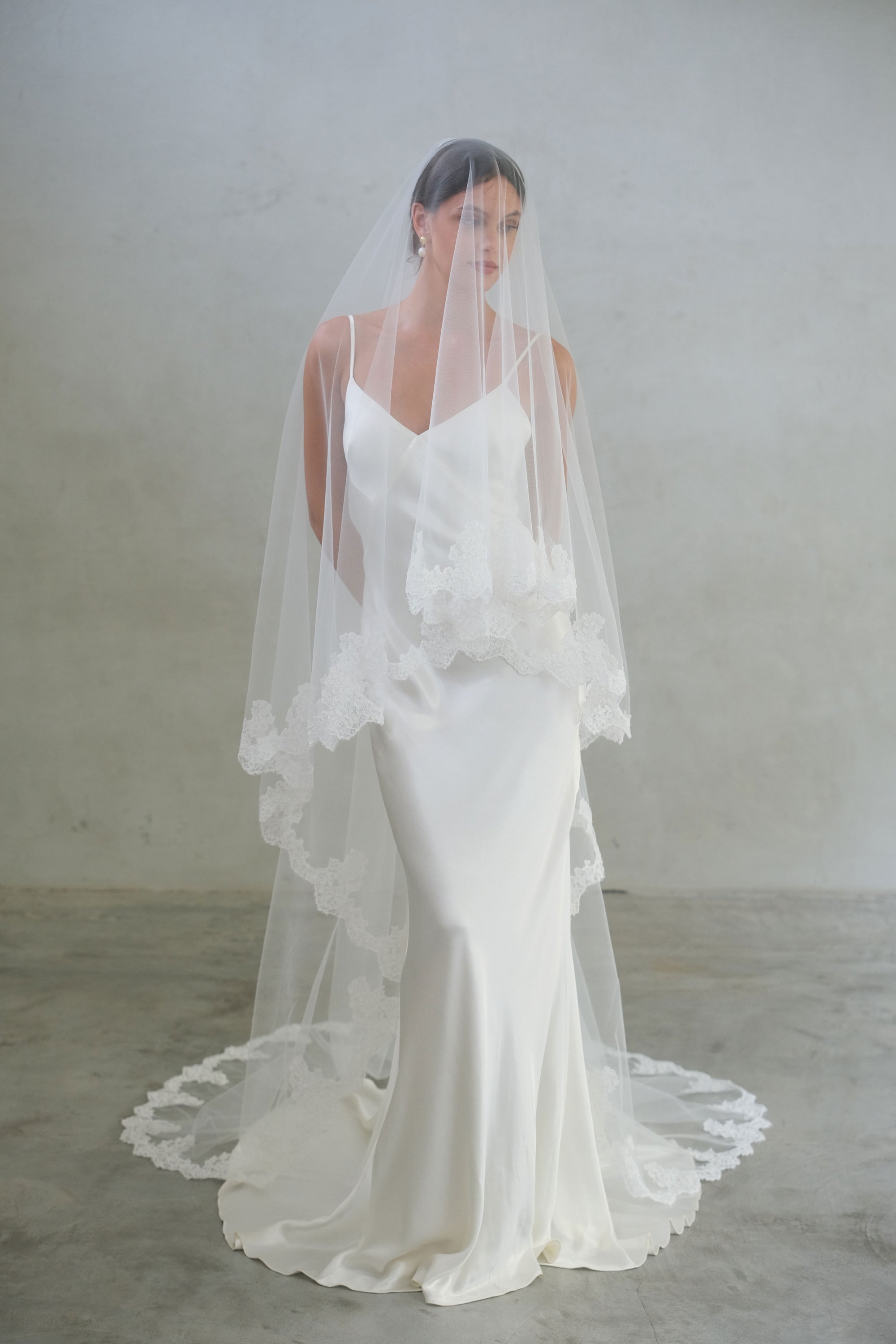 Full length front facing bride wears long, two-tier wedding veil with lace edging and blusher down 