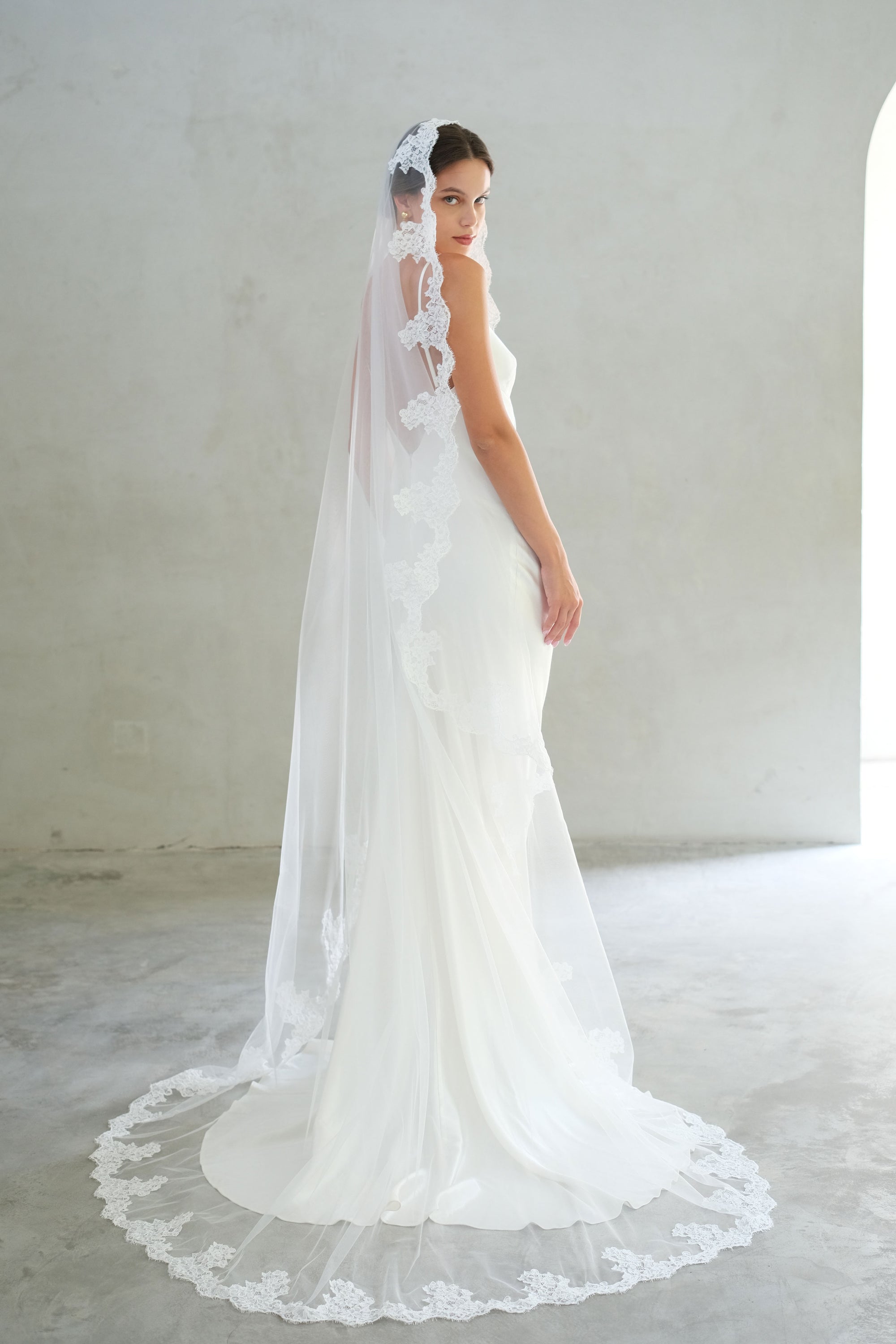 Full length shot of bride turning to show lace trim on edges and all around train of long, mantilla style veil