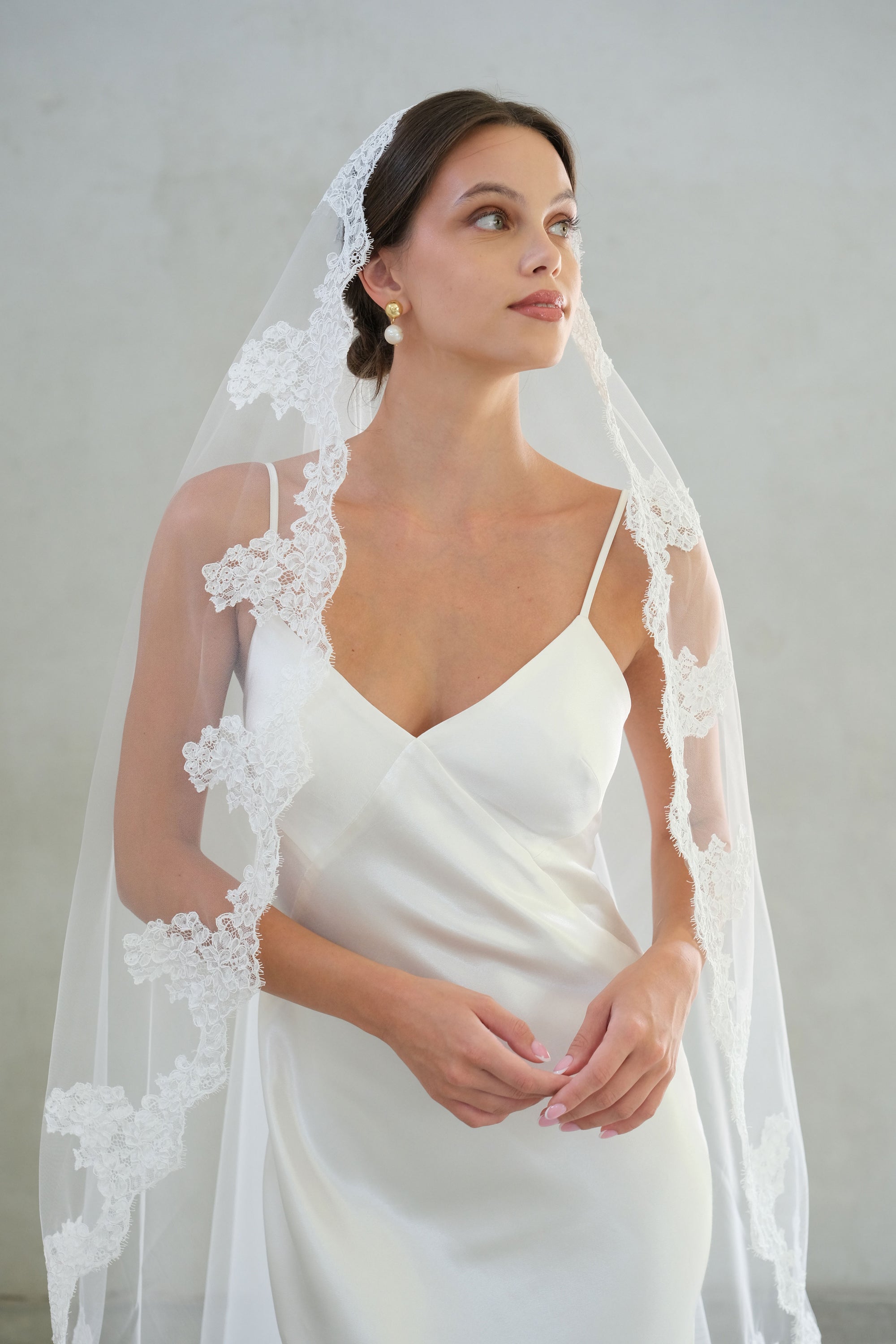 Front facing bride wears long mantilla style veil with lace trim