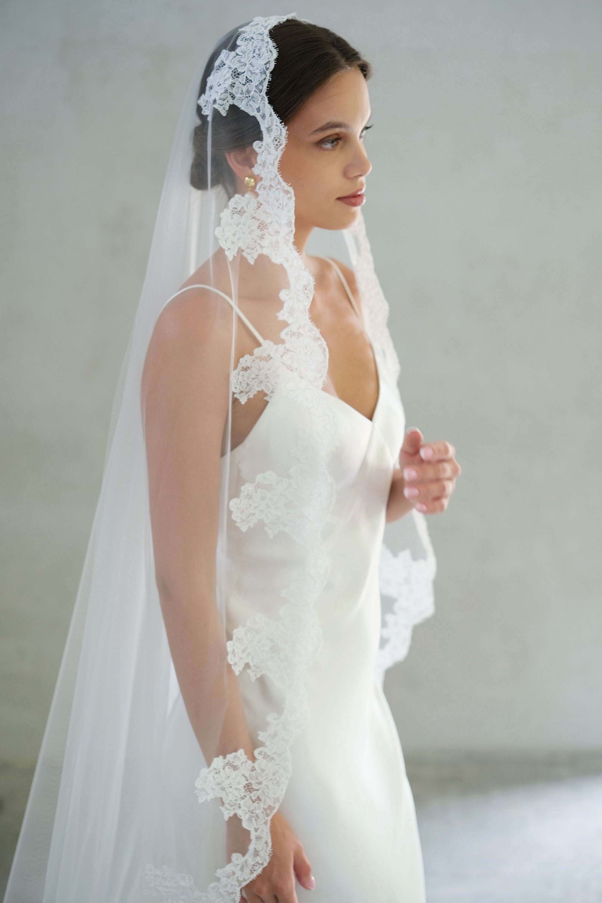 Half length bride in profile wears lace edged mantilla veil