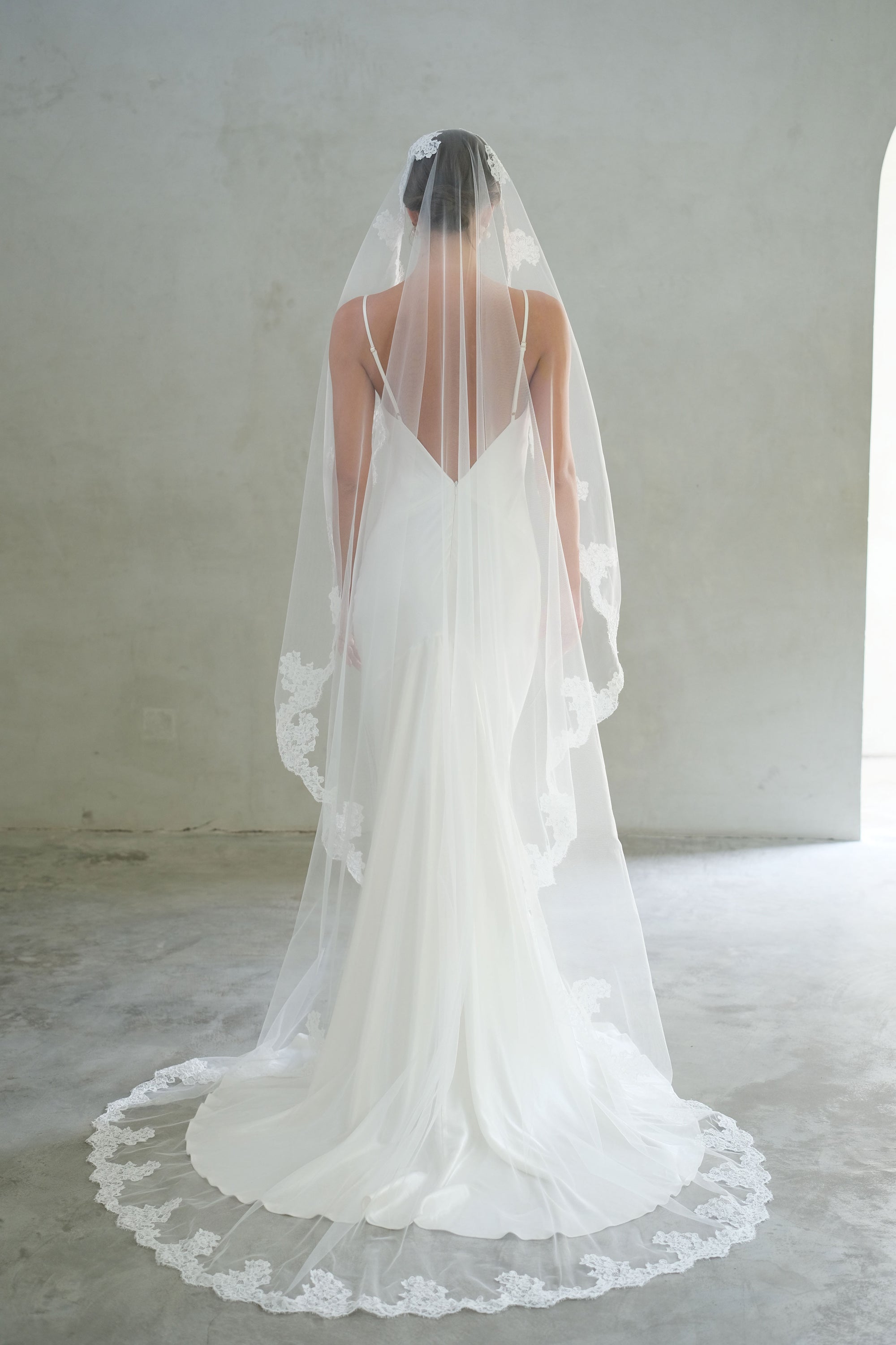 Full length back view of bride wearing long lace trimmed mantilla veil
