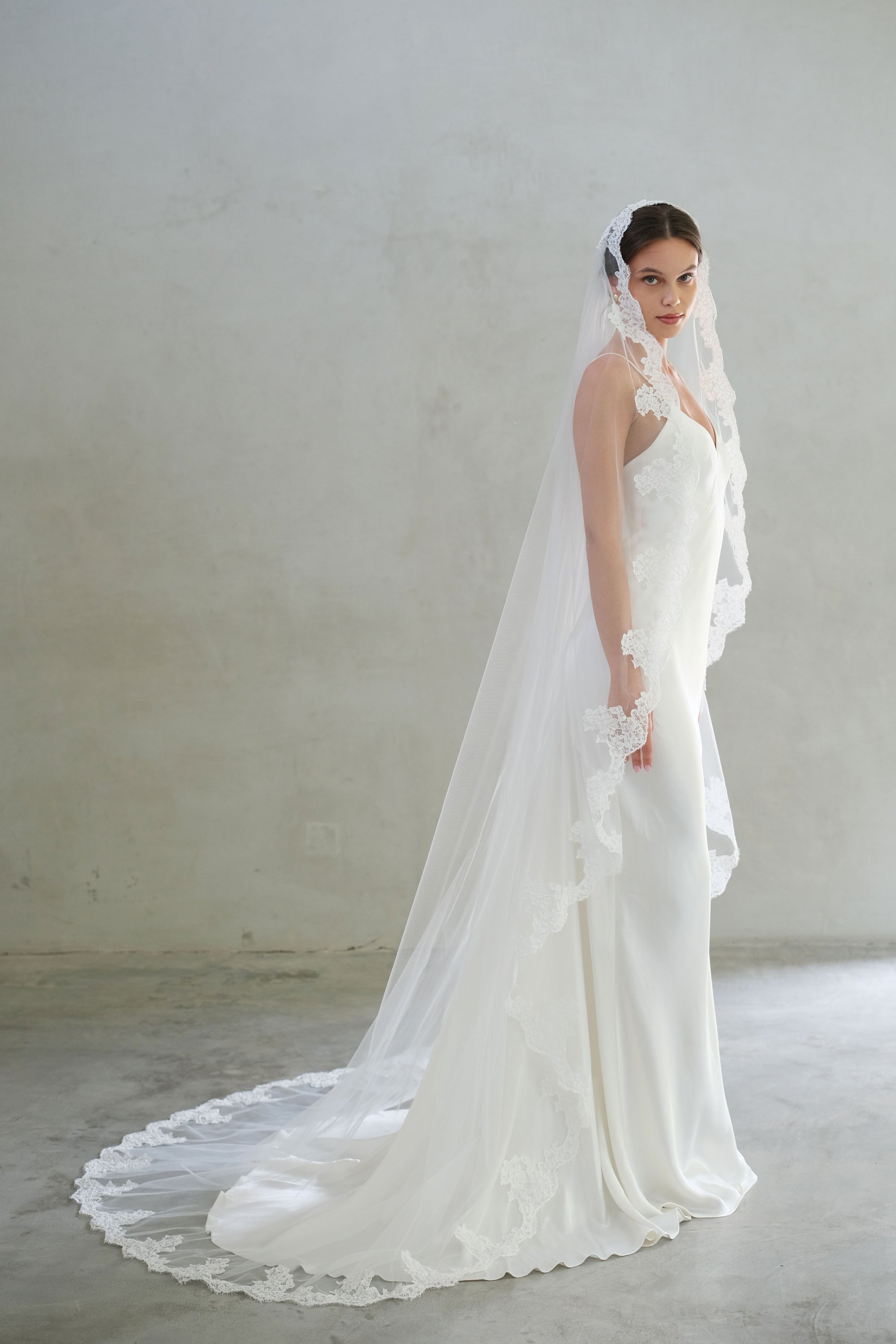 Full length side view of bride wearing chapel length lace trimmed mantilla veil