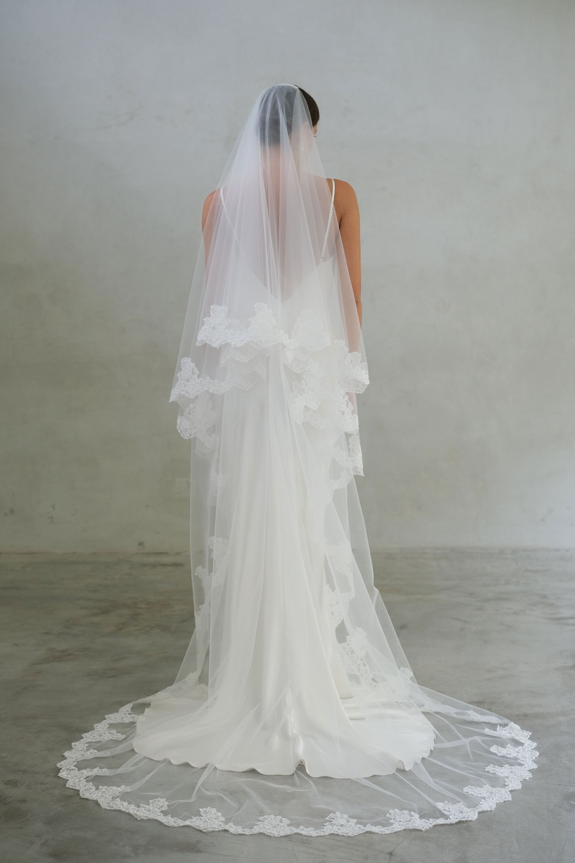 Full length back view of bride in modern lace edged wedding veil; chapel length; blusher off