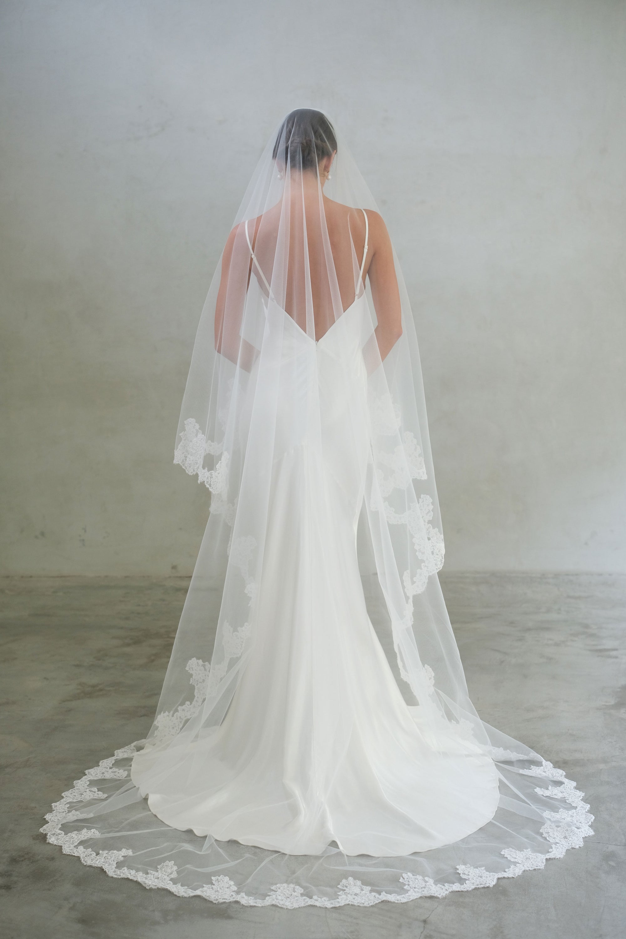 Full length back view of long, two tiered wedding veil featuring lace edging
