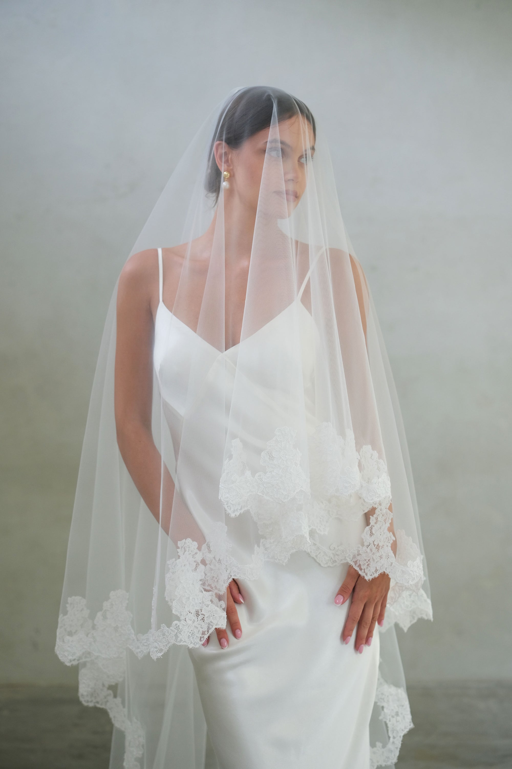 Front facing bride wears laced edged wedding veil showing blusher down