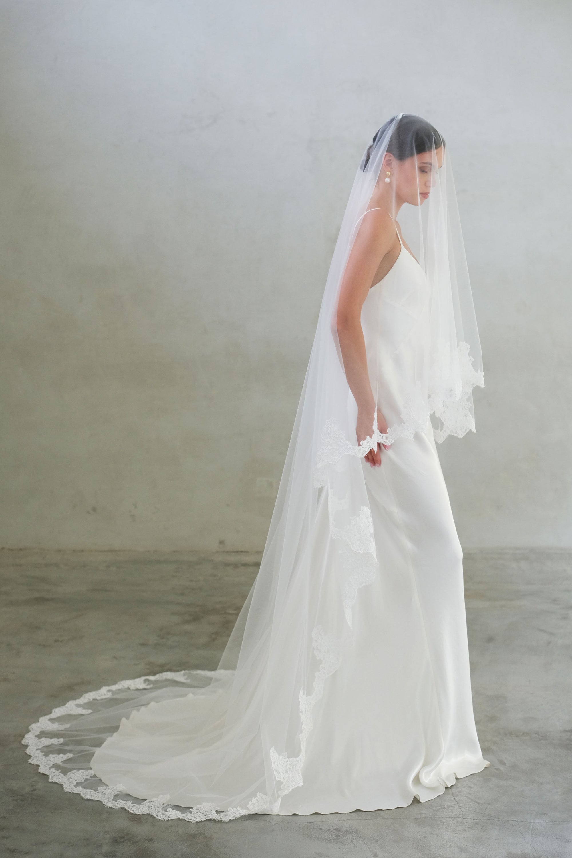 Full length bride in profile wears two-tier, lace trimmed veil in chapel length
