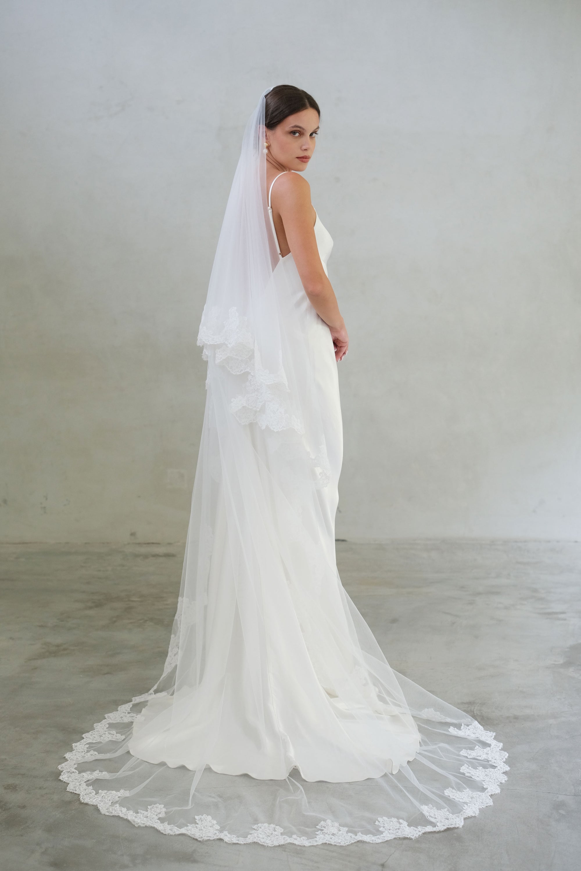 Full length shot of bride turning to show modern laced trimmed wedding veil in chapel length with blusher off
