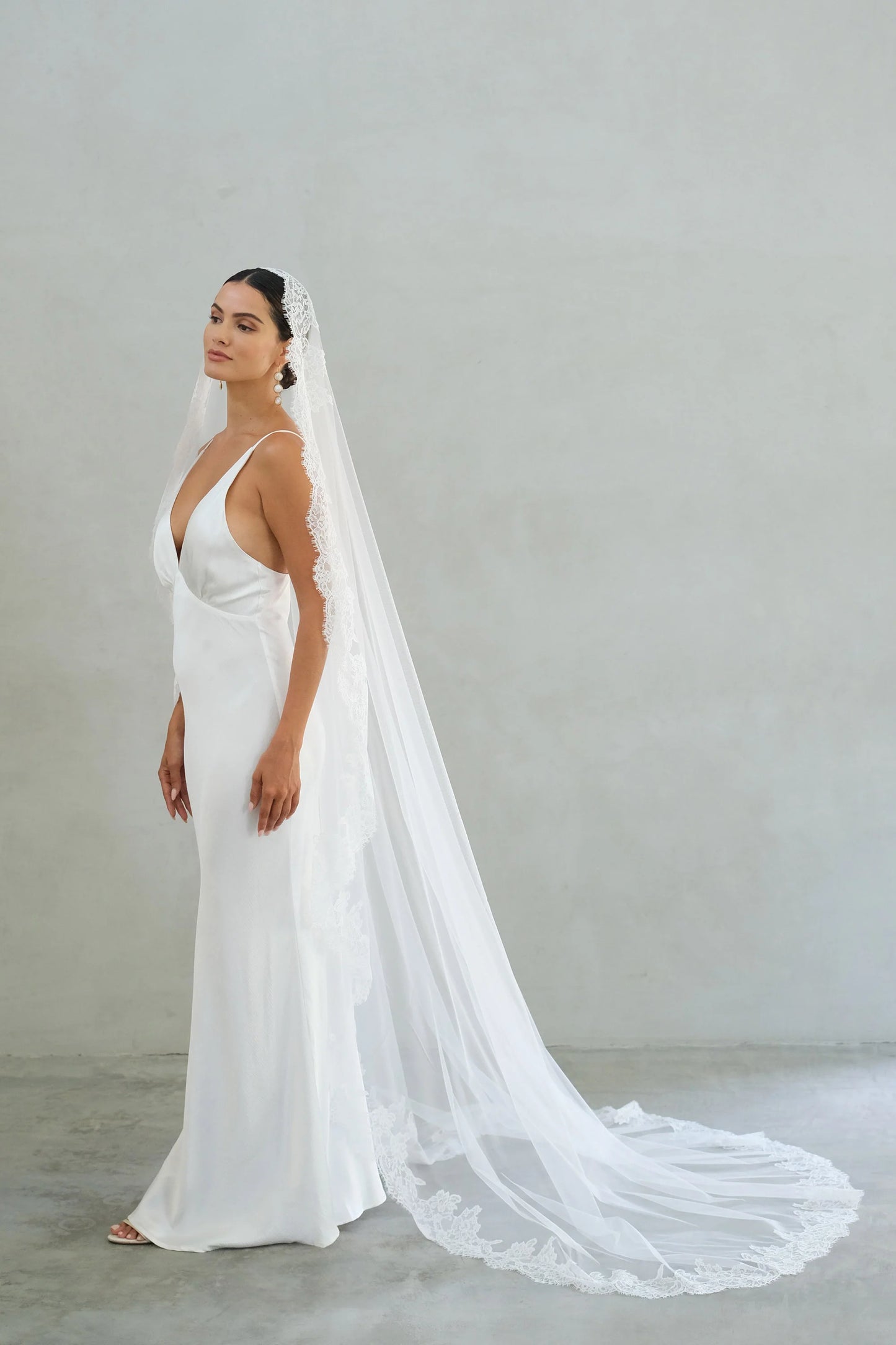 Full length side view of bride modelling long, lace trimmed mantilla veil