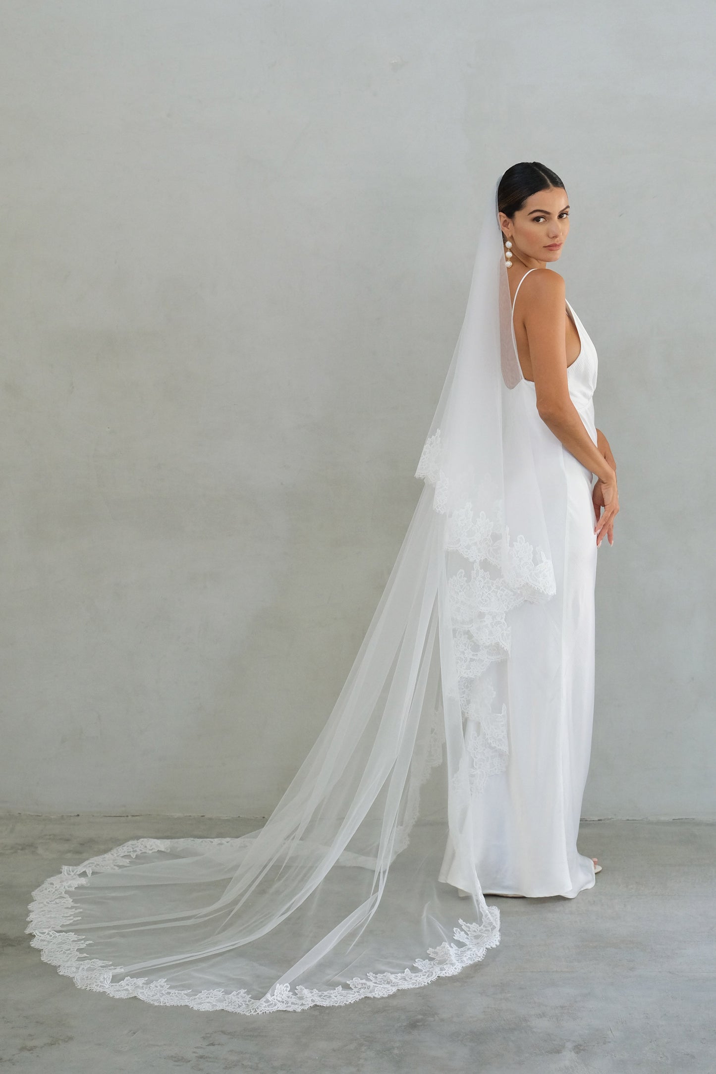 Full length side view of bride wearing long two tier lace trimmed veil shown with blusher off 