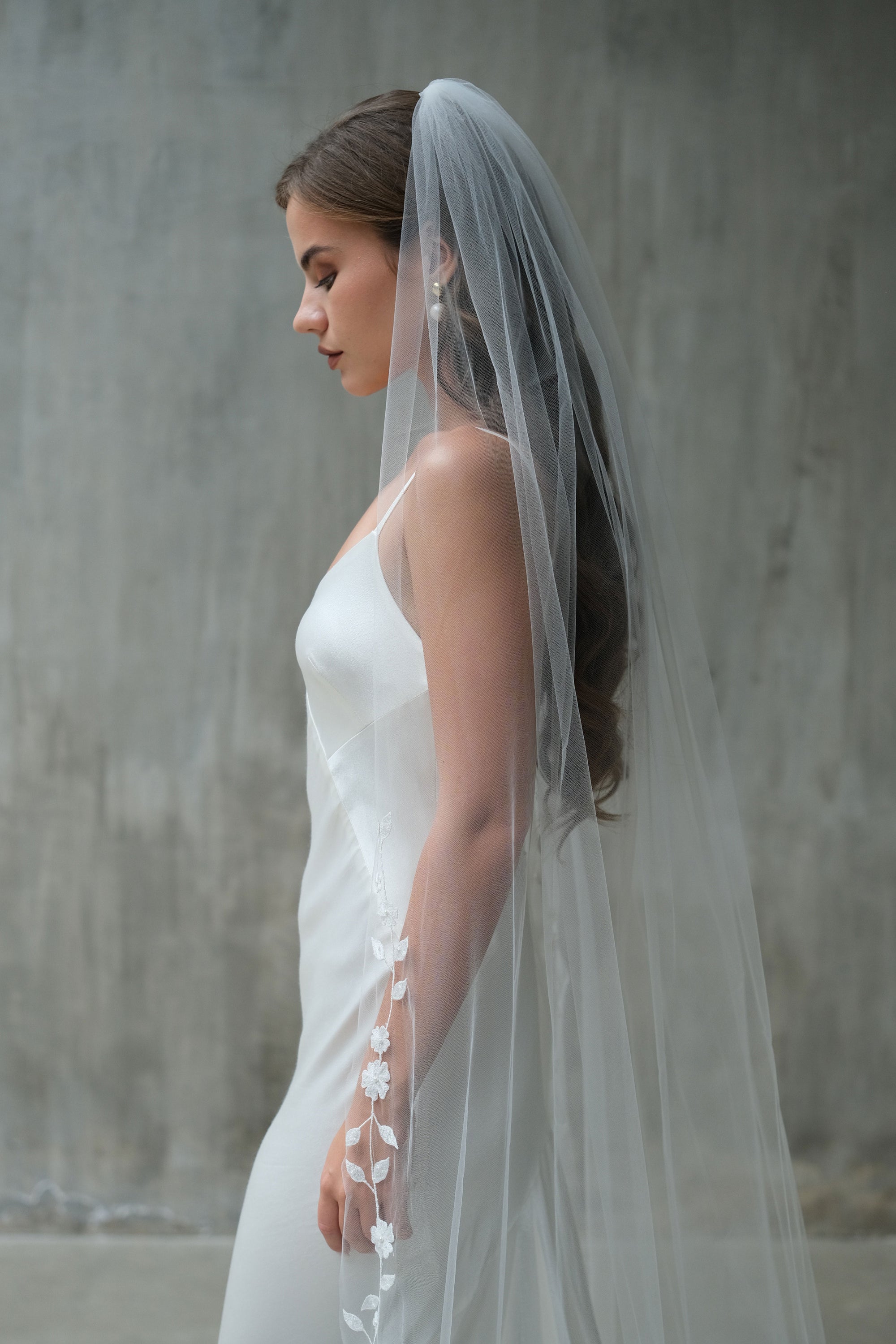 Bride in profile wearing veil gathered at the comb and embroidered with delicate flowers at the edge