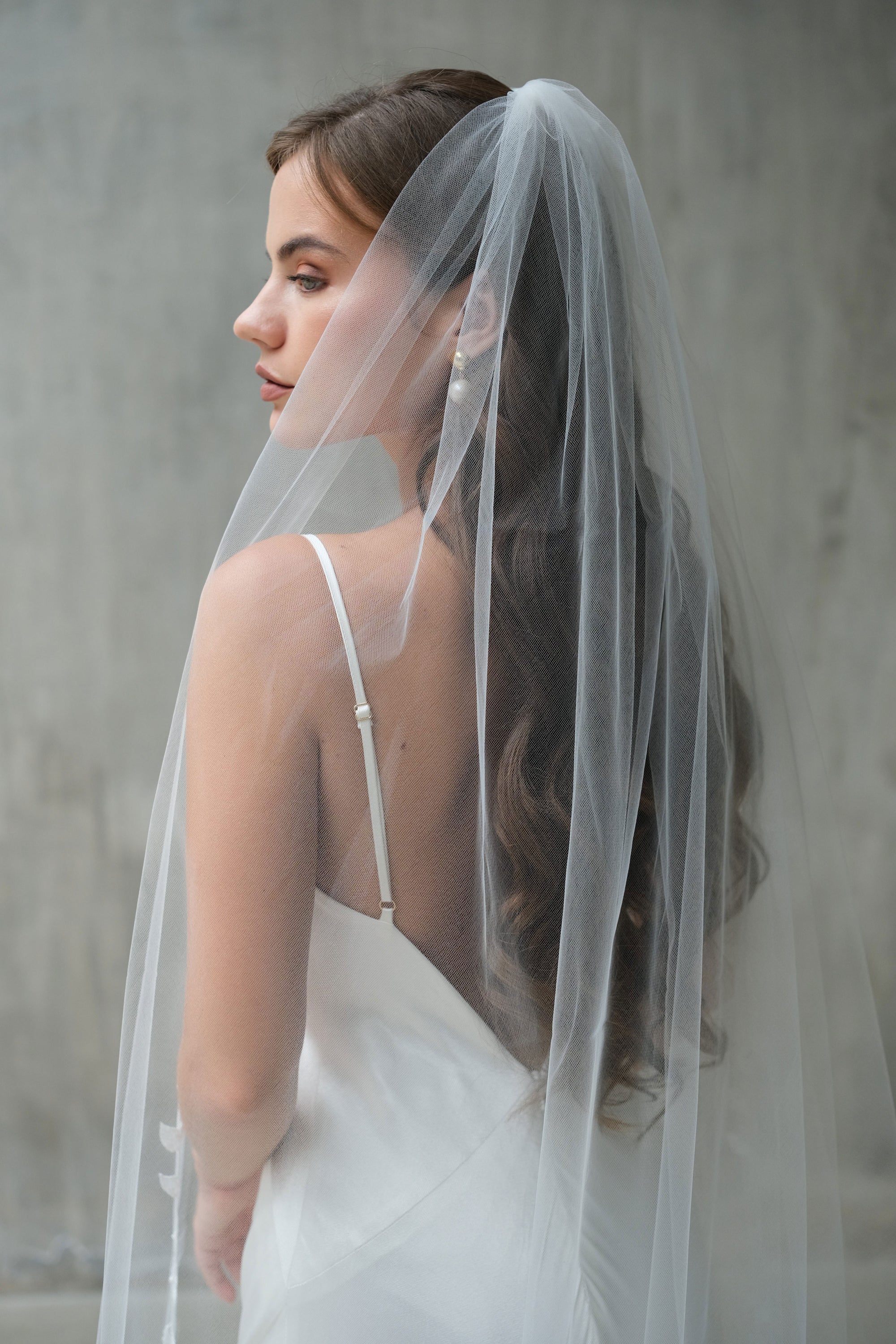Single-tiered, long lightweight tulle bridal veil drapes over the head and shoulders to complement a loose romantic hair styling