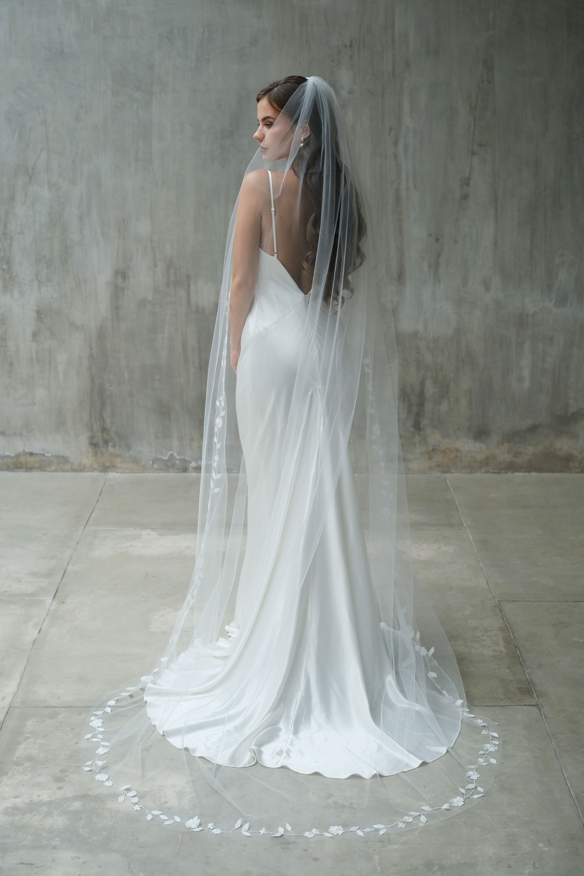 Full length back view of bride wearing long, single tier bridal veil, gathered at the comb and featuring delicate floral embroidered edging