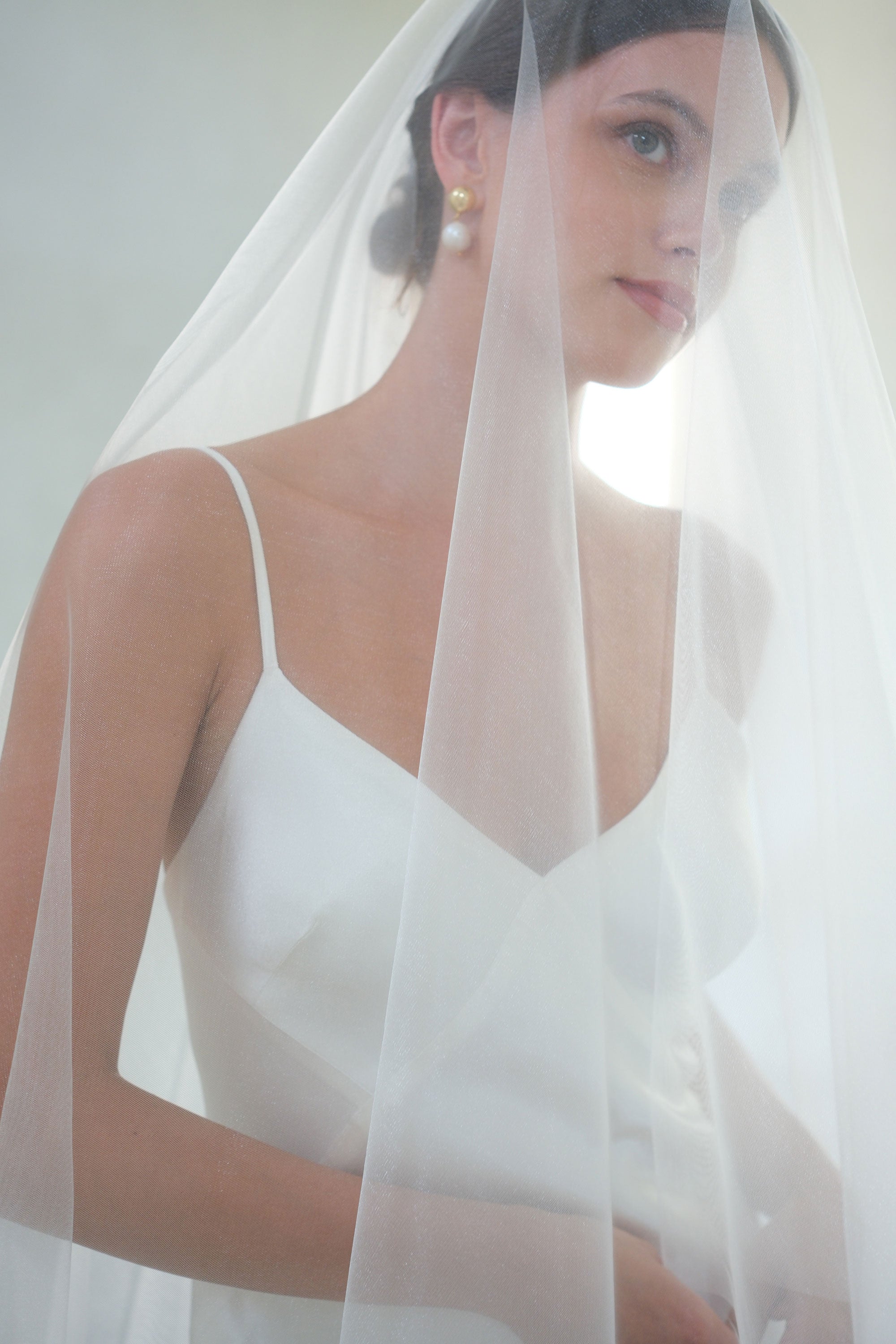 Head and shoulders bride wears shimmer tulle wedding veil, blusher down