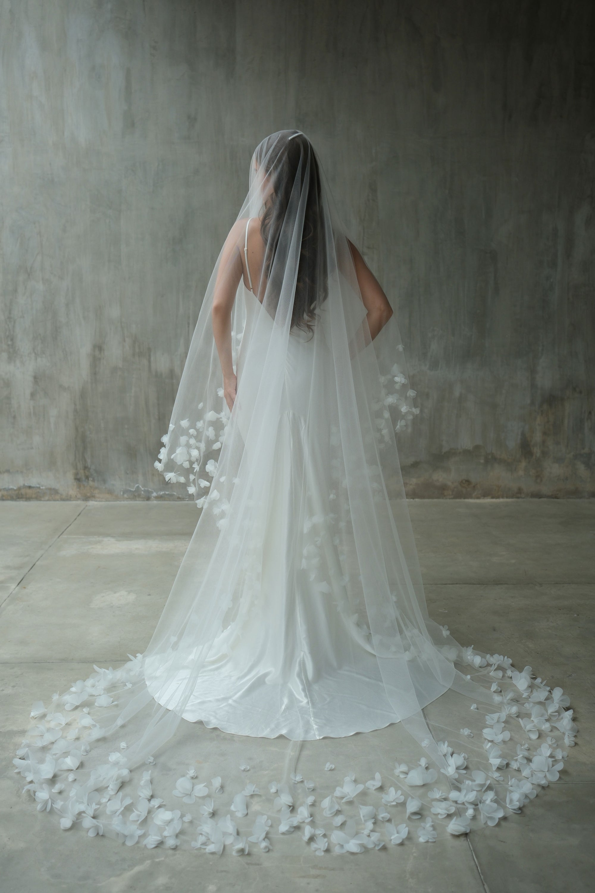 Full length back view of bride wearing long veil edged with fabric flowers