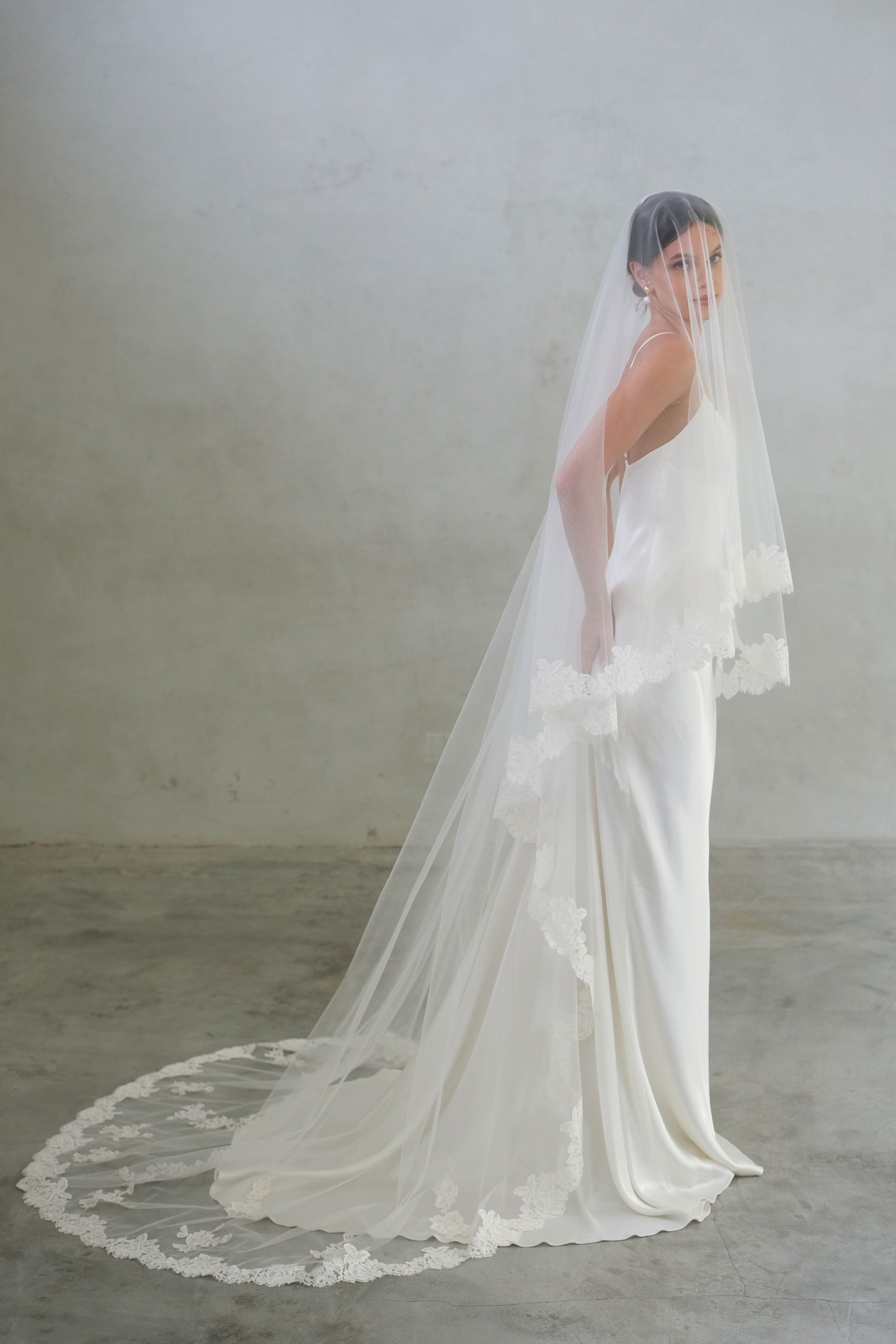 Full length side view of long sheer, two-tiered bridal veil with lace edging and scattered floral applique around train