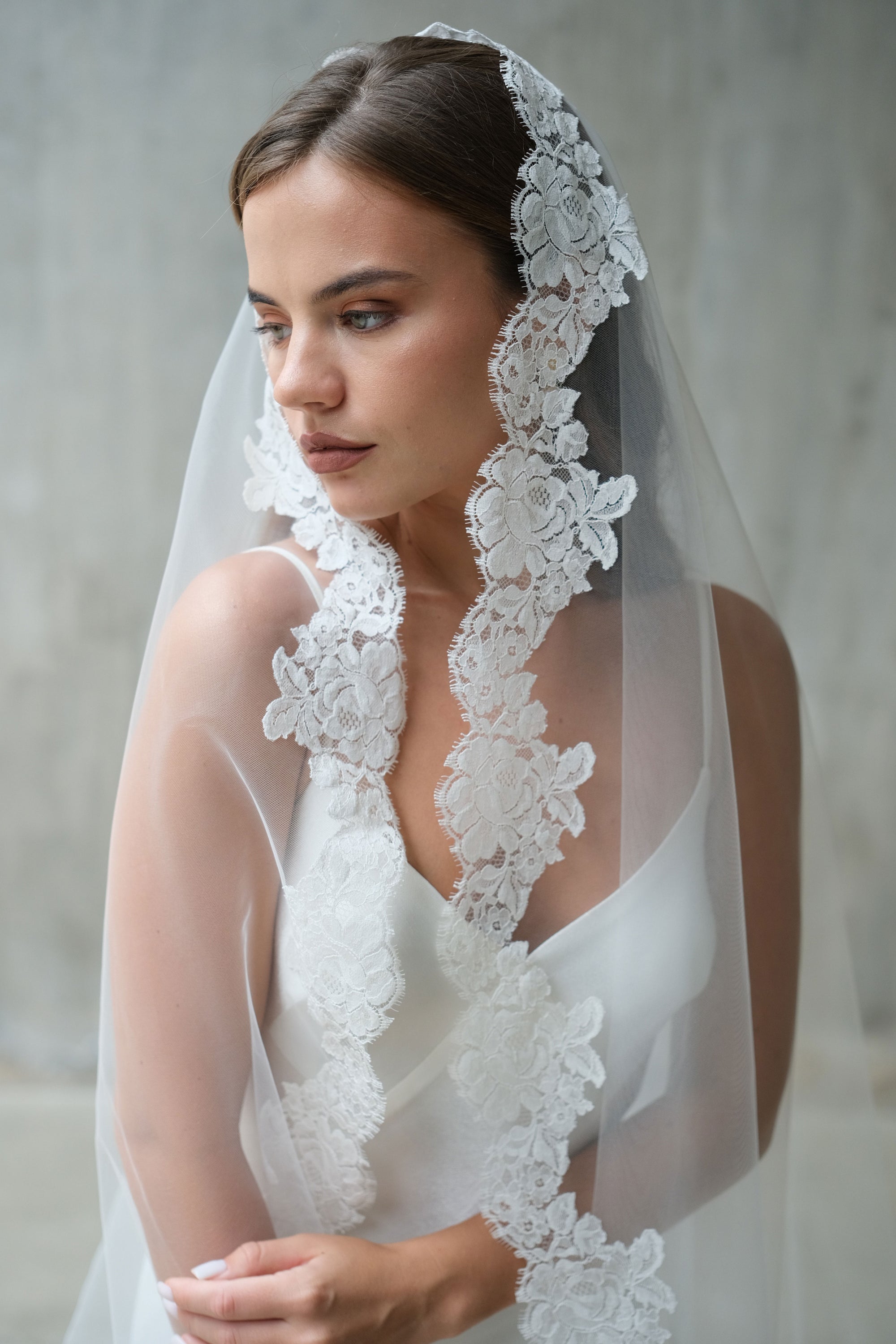 A bride wearing a sheer one-tier mantilla wedding veil, a modern veil veil in cathedral and chapel length