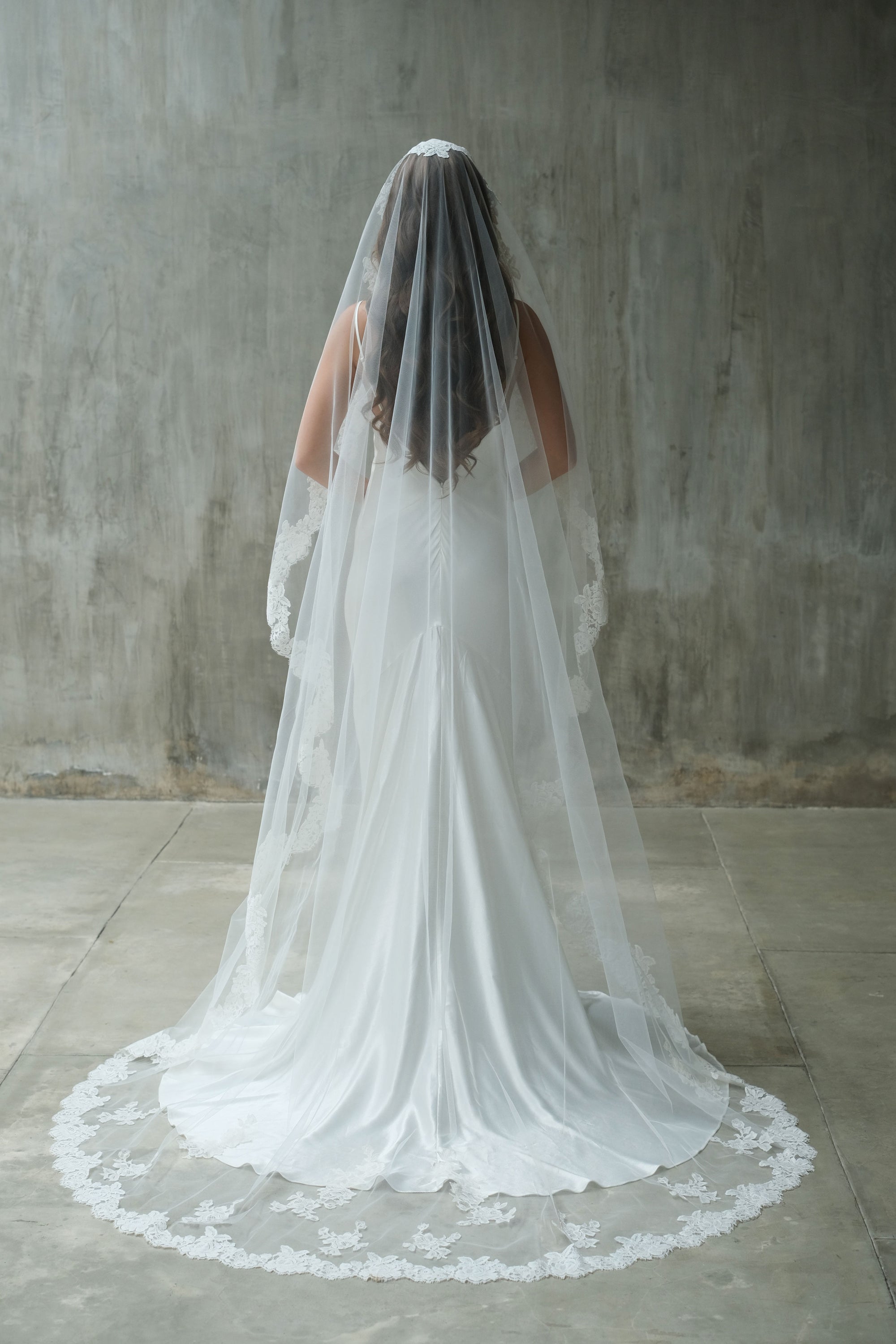Full-length back side photo of a bride wearing one-tier long mantilla wedding veil with lace edge