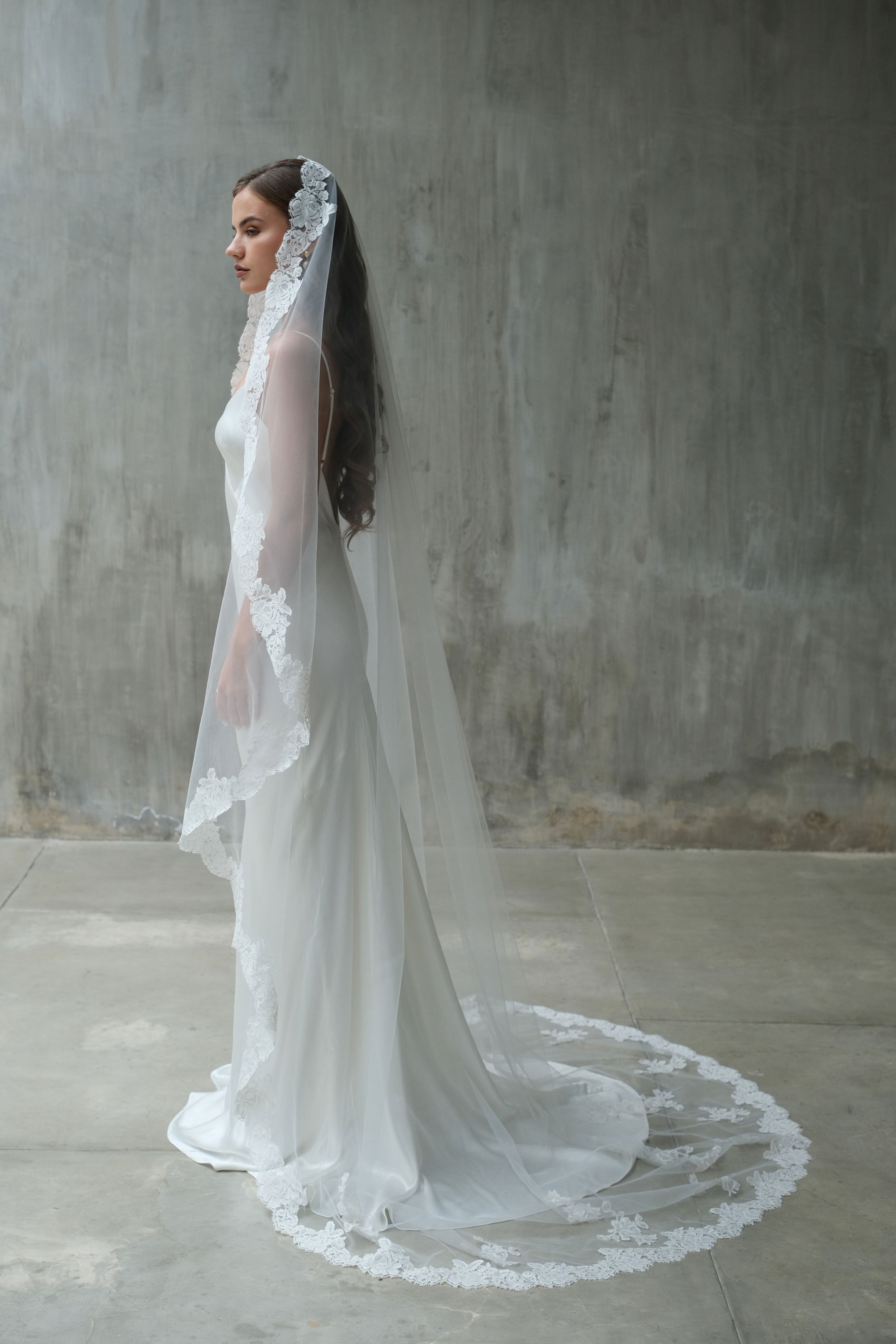 Full-length side profile photo of a bride wearing one-tier mantilla lace edge veil in chapel length