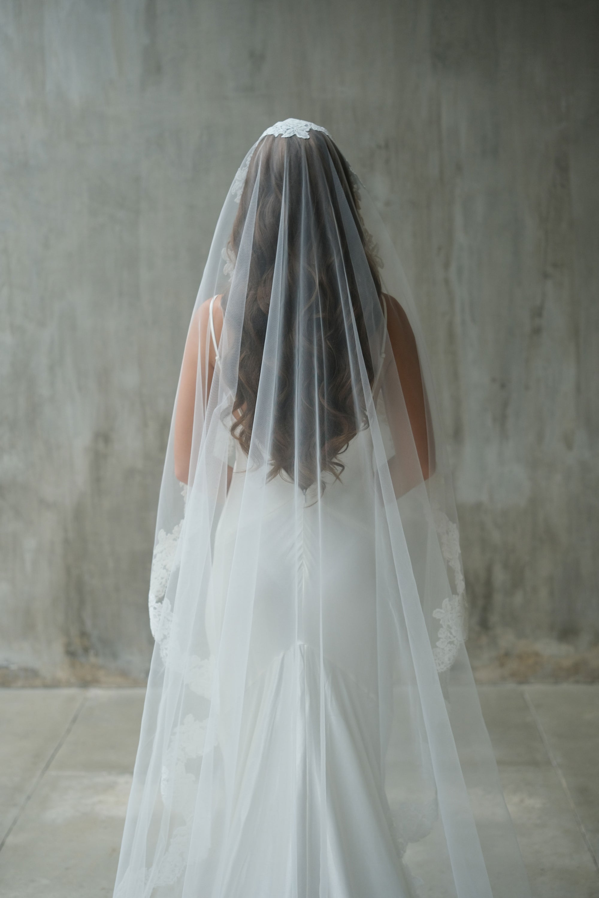 Back side photo of a bride wearing one-tier mantilla wedding veil with lace edge