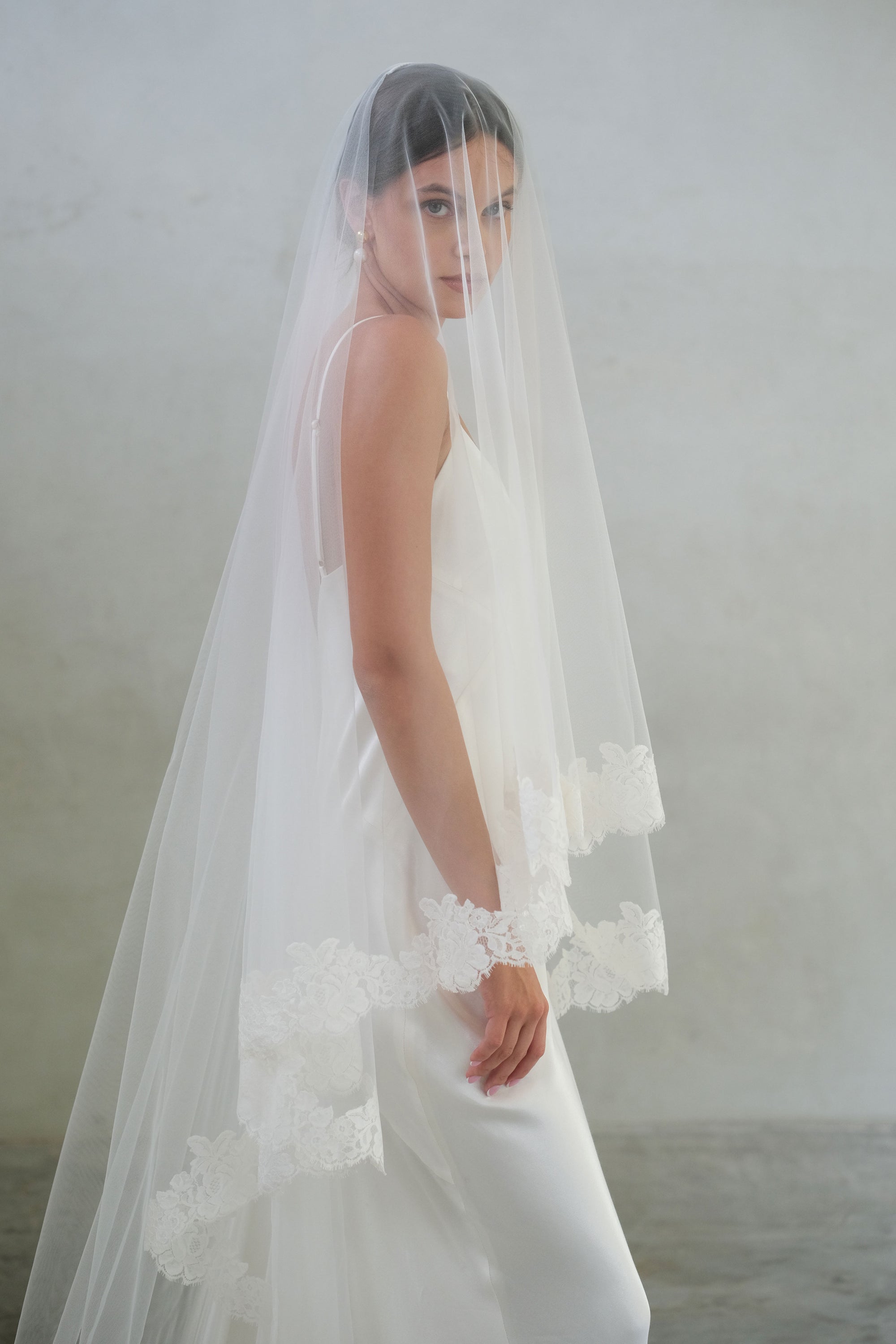 Side view of bride wearing long sheer veil with blusher and floral lace edging