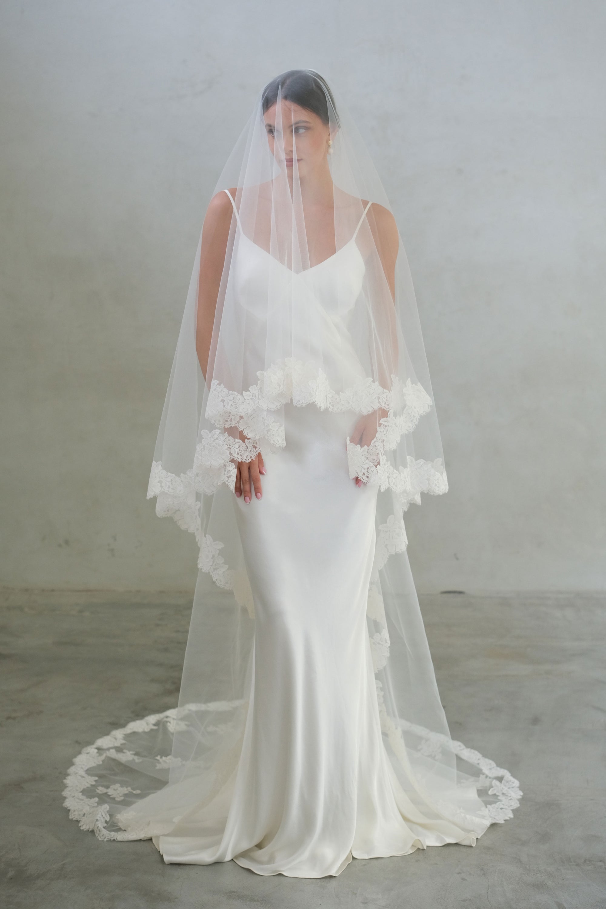 Full length front facing bride wears two-tiered, long veil with lace edging and floral appliques around train