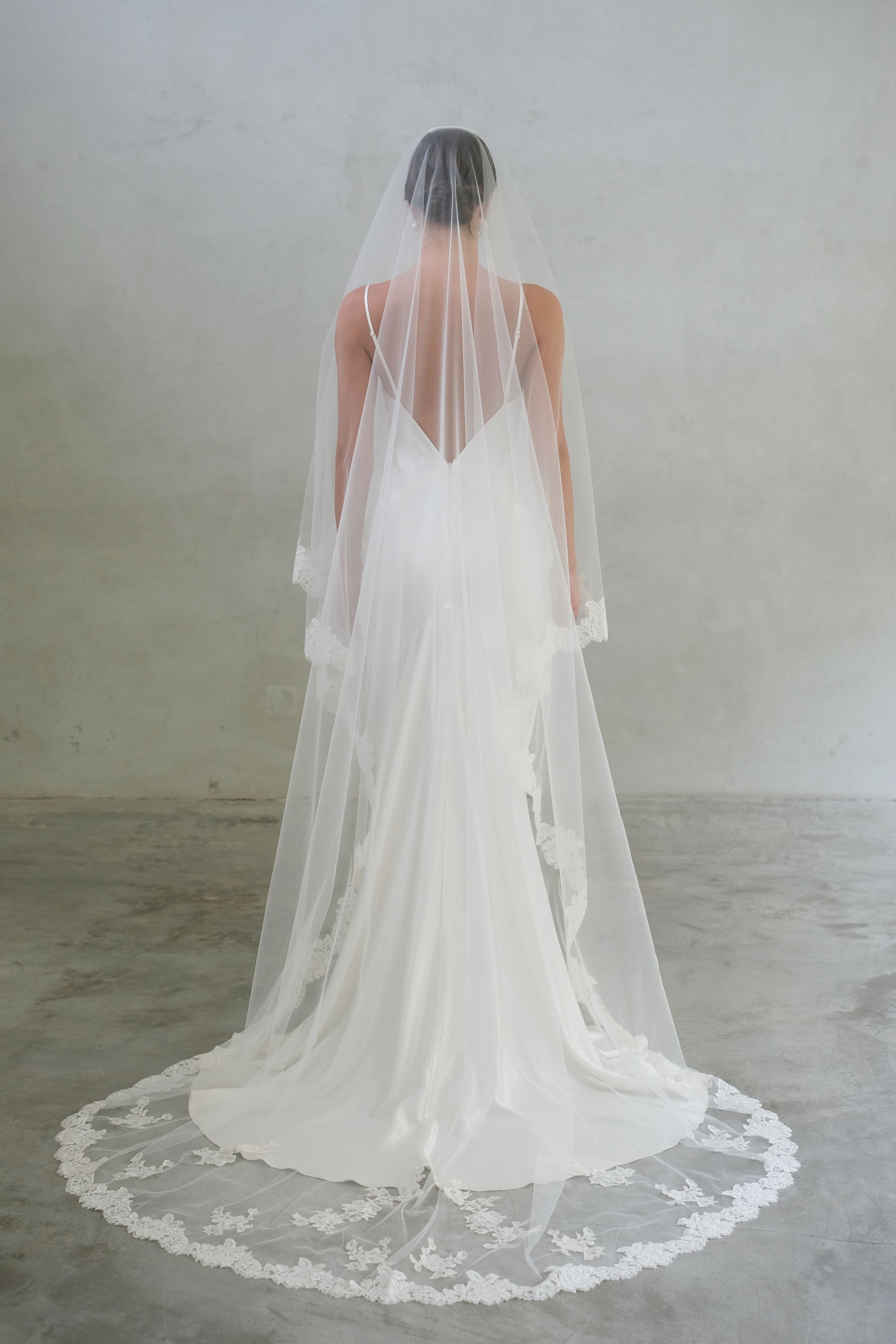 Full length back view of bride wearing laced-edged long veil featuring floral appliques scattered around train