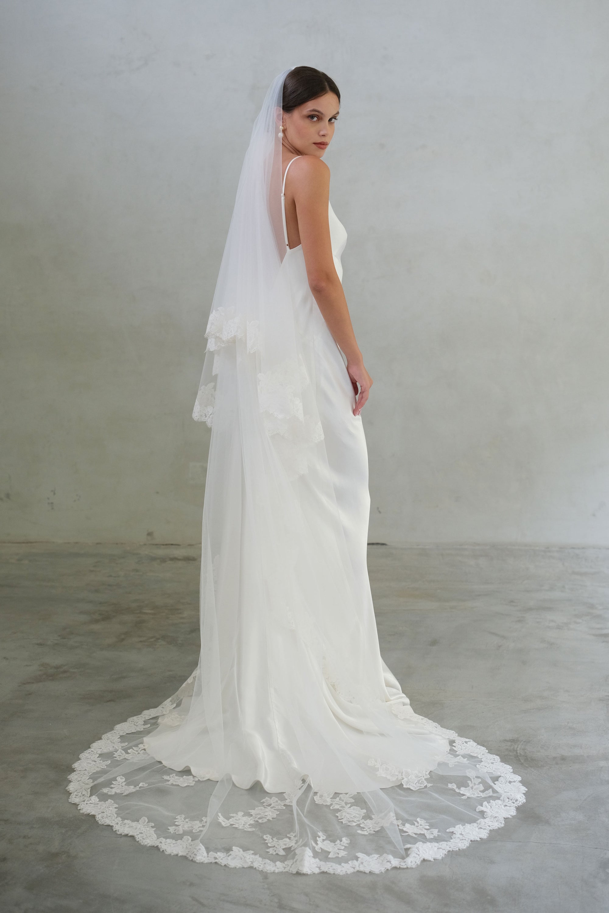 Full-length side view of bride wearing long, lace-edged, two-tiered veil. Floral applique details are scattered around the train.