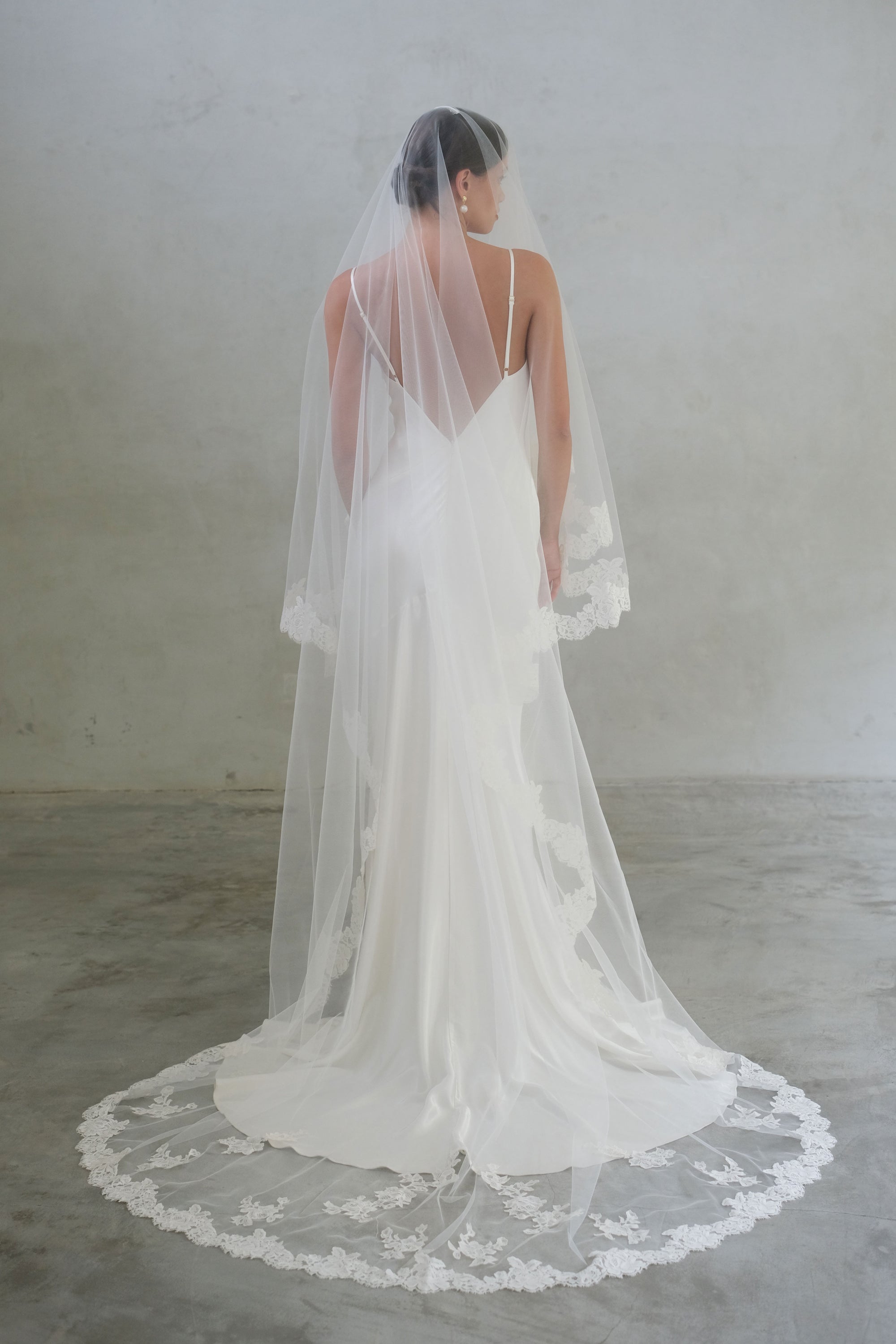 Full-length back view of bride wearing long, lace-edged, two-tiered veil (with blusher) featuring scattered floral applique work around the train