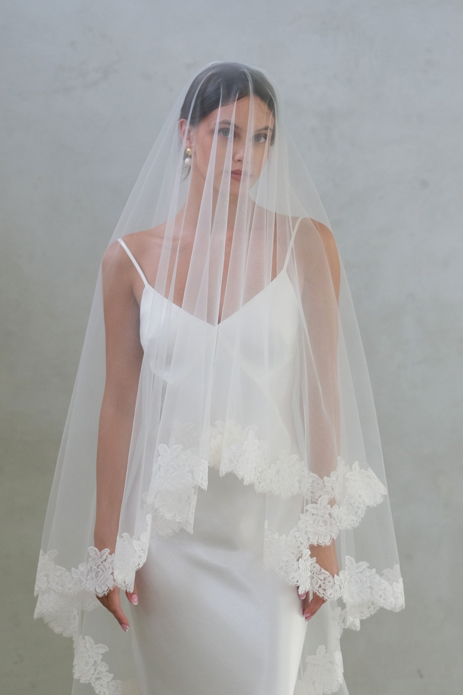 Front facing bride wears long veil with blusher, featuring floral lace edging