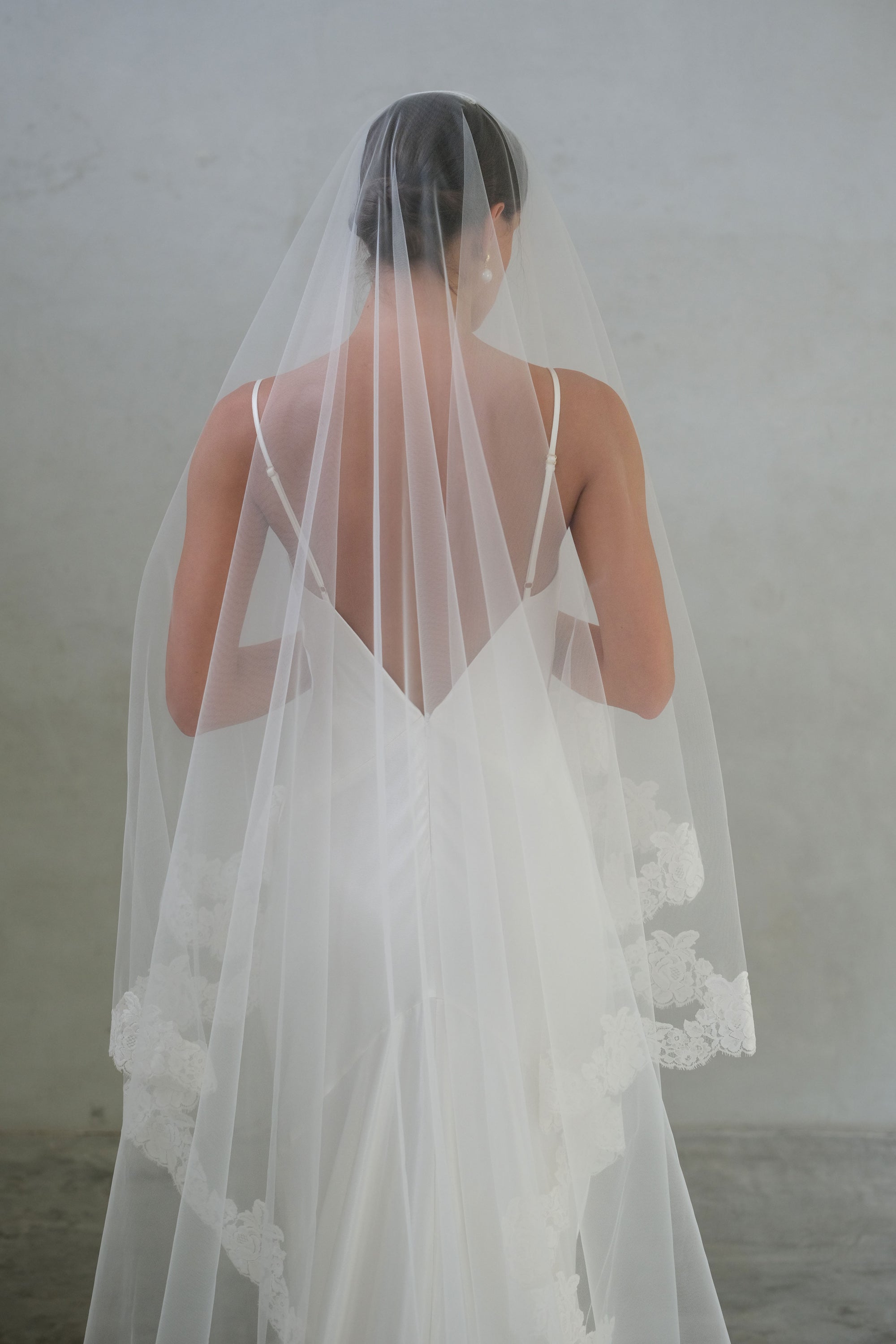 Mid-length back view of bride wearing lace-edged, two-tiered veil (with blusher)