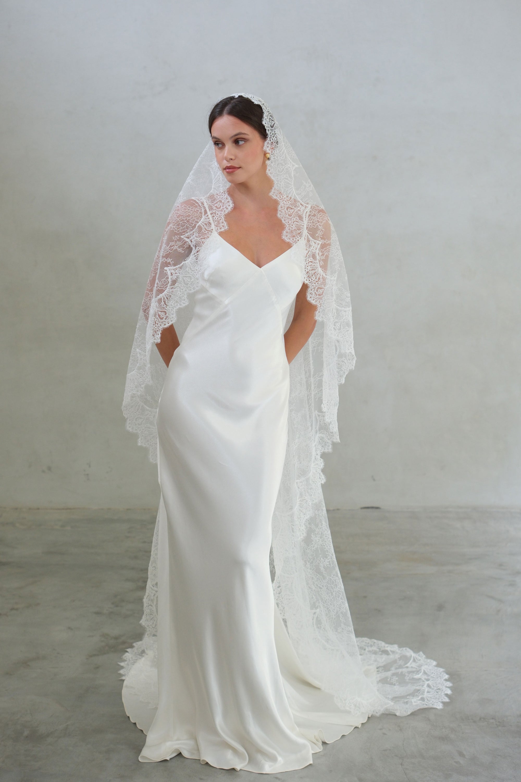 Full length front facing bride wears fine lace long mantilla veil draped over shoulders
