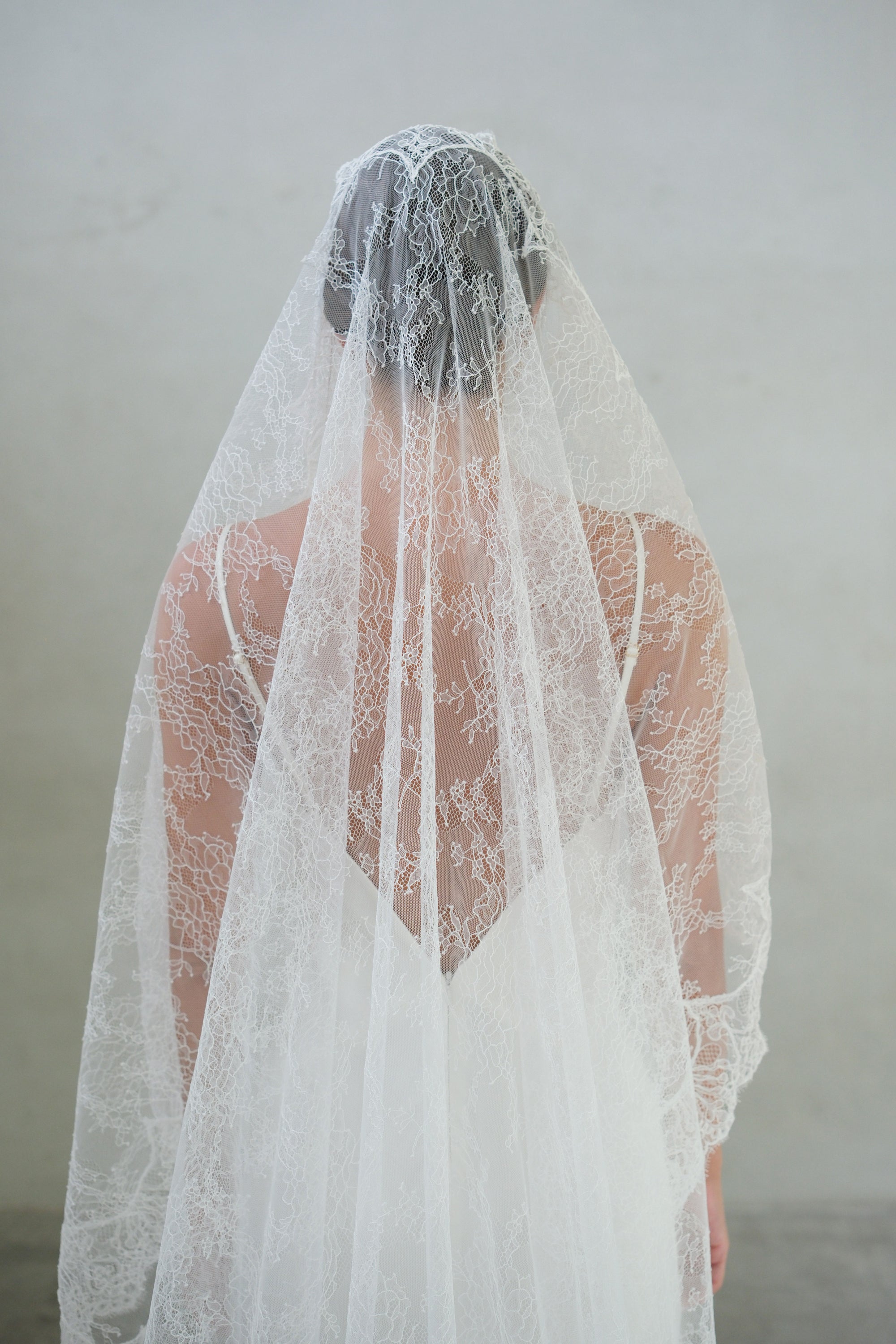 Back view of fine lace bridal veil cascading over the head and shoulders of model