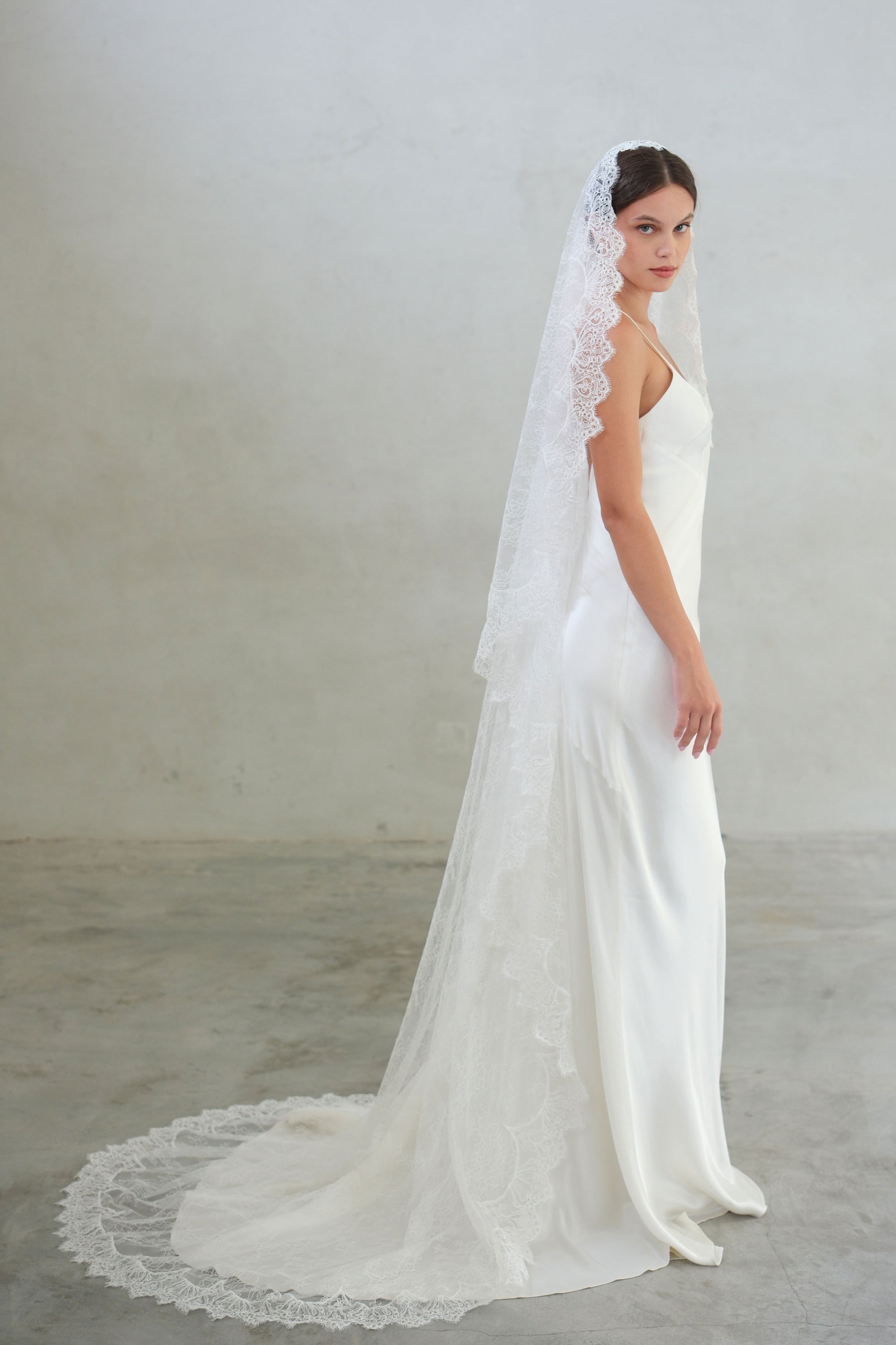 Full length side view of bride wearing long mantilla style veil in sheer floral lace with scalloped lace edging