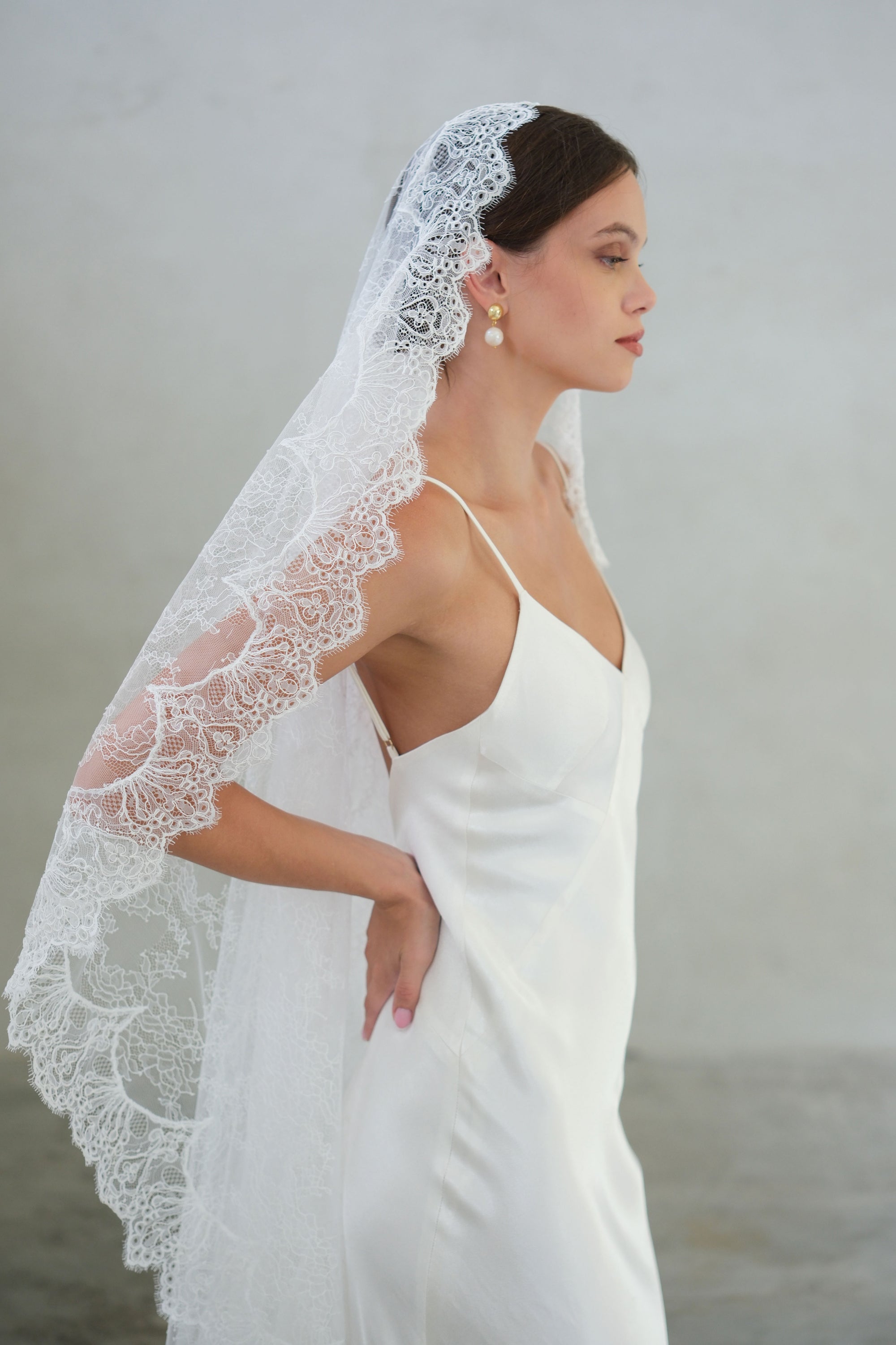 Bride in profile wears full sheer lace mantilla veil finished with scalloped lace edging