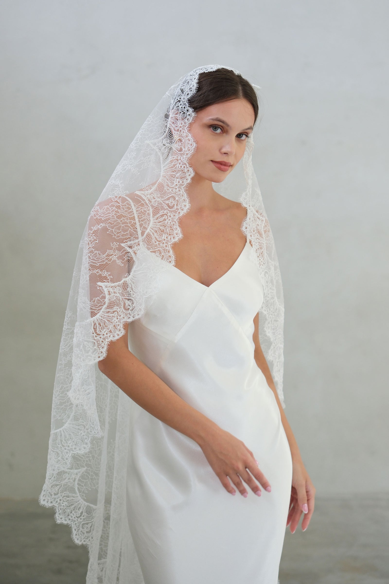 Bride wears delicate sheer lace mantilla veil with scalloped lace edging