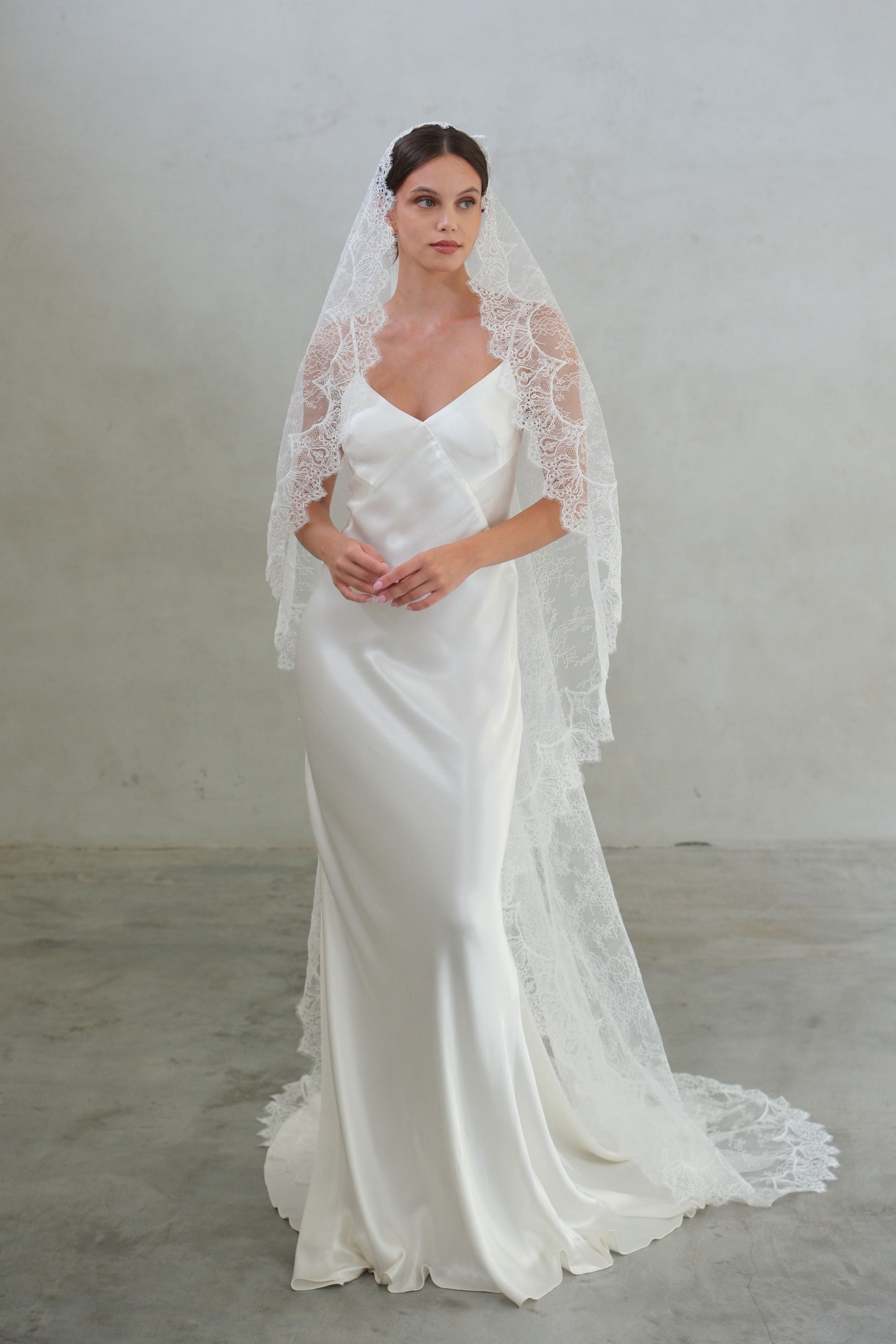 Full length front facing bride wears long mantilla veil hand crafted from sheer full lace fabric with scalloped floral lace edging
