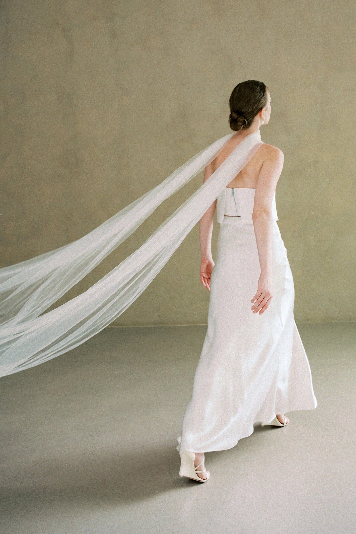 Full length back view of bride wearing soft tulle wedding scarf flowing out behind as she walks