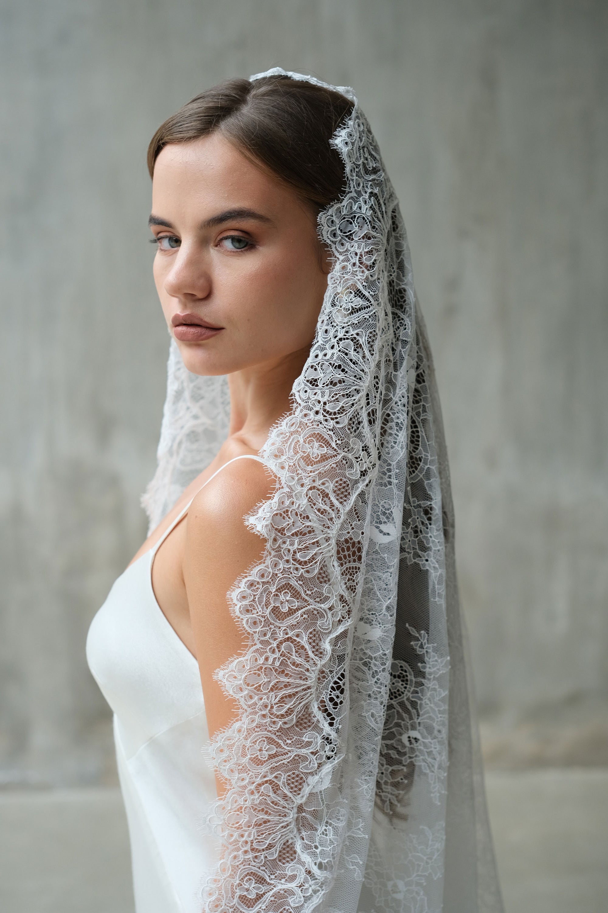 Bride turns to show lace detail of tradtional style mantilla wedding veil draped over hair and shoulder