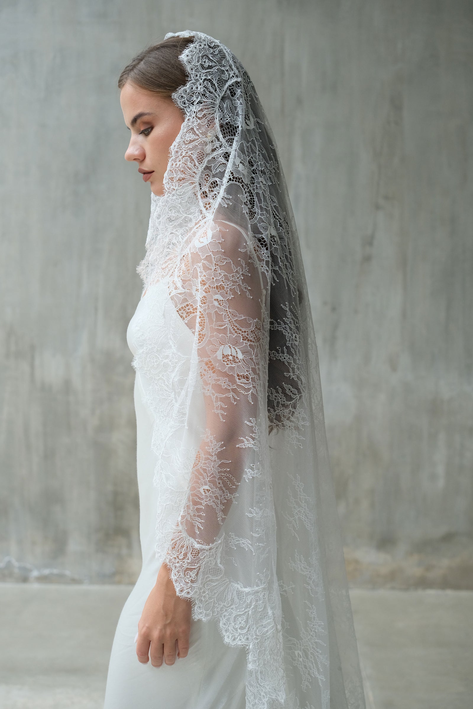 Bride in profile wears a soft, sheer full lace mantilla veil with scalloped lace edging