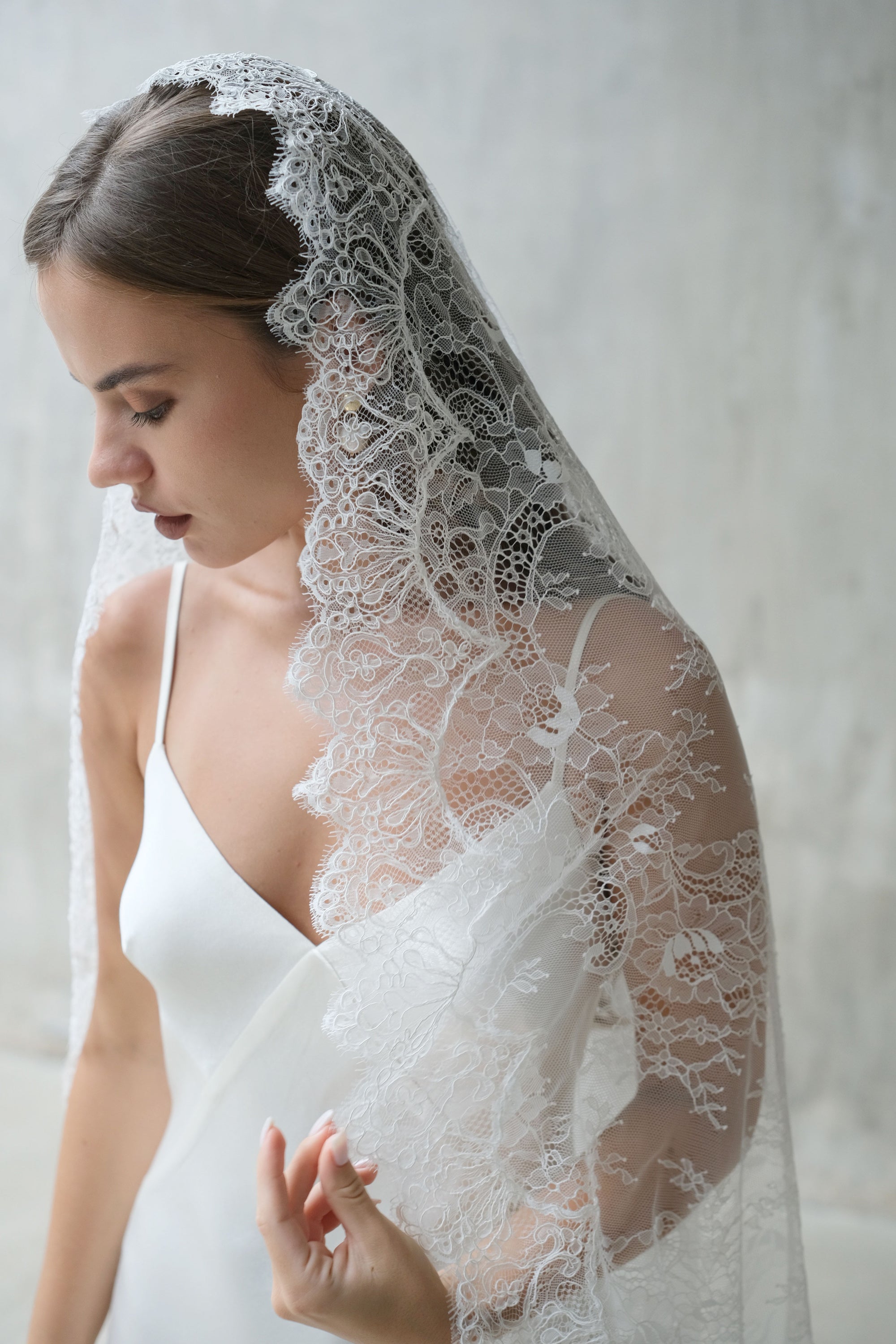 Sheer lace mantilla veil drapes over the hair and shoulders of minimally-styled bride