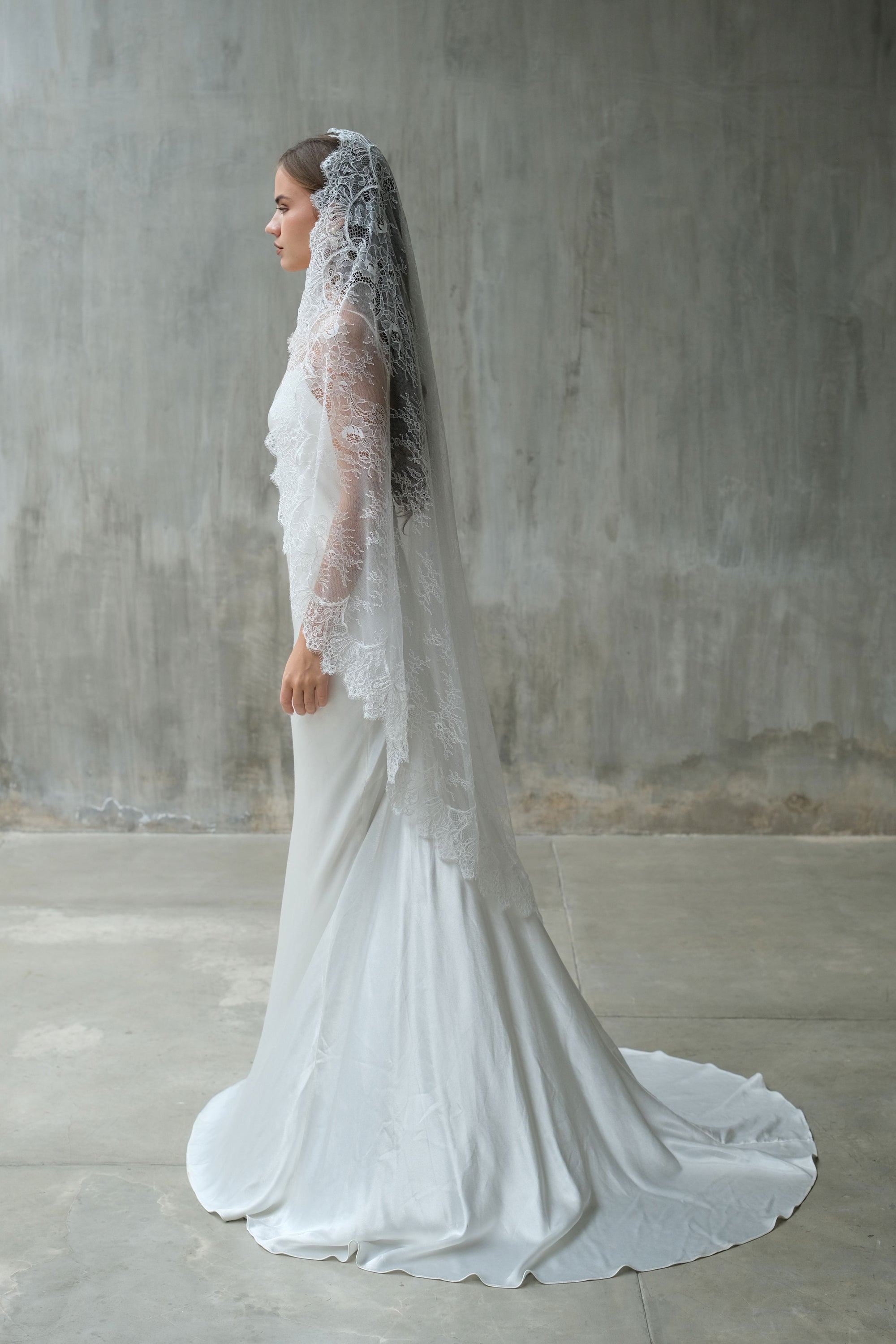 Full length bride in profile wears tradional style full lace mantilla wedding veil - mid (waltz) length