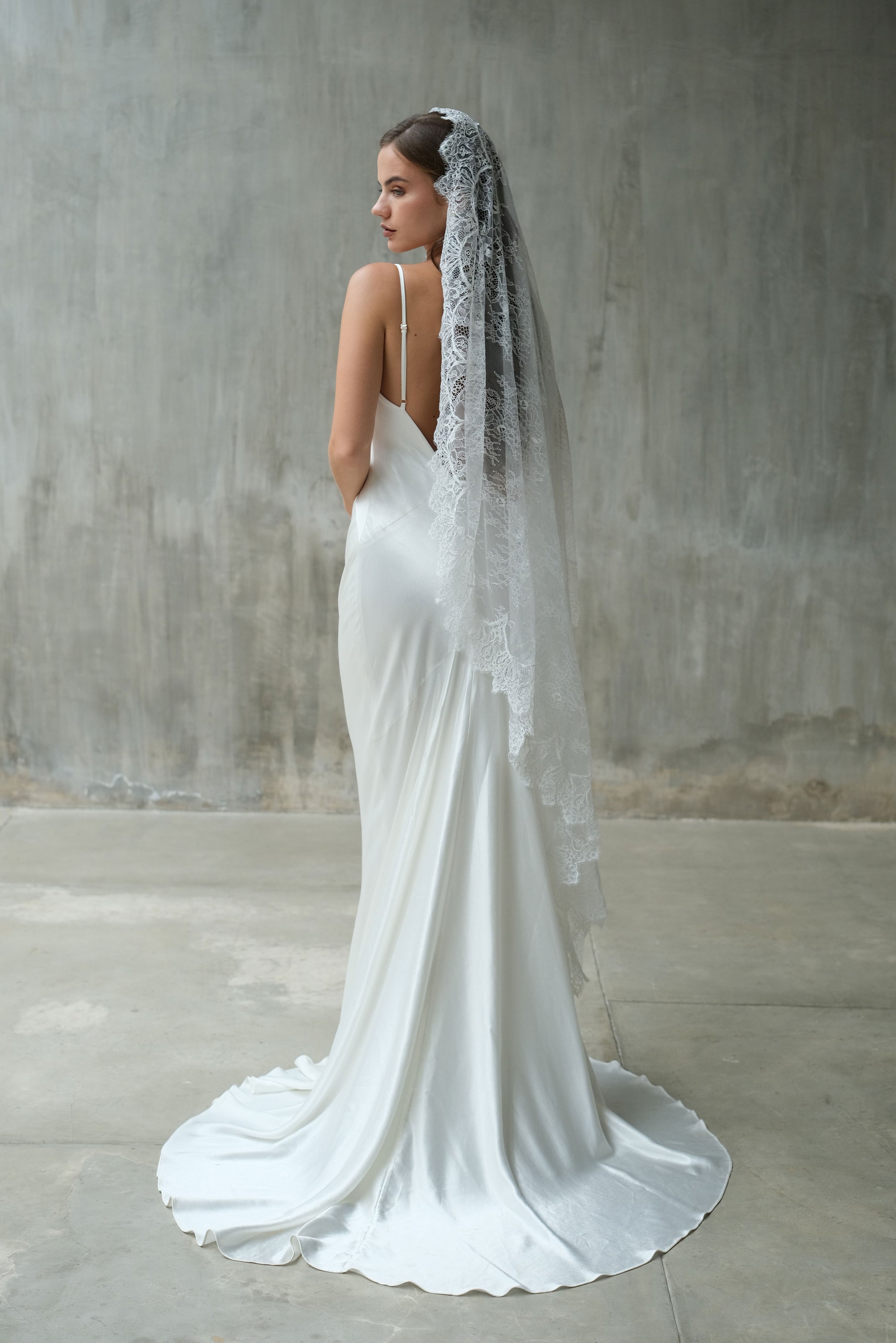 Full length bride in profile wears waltz length lace mantilla veil