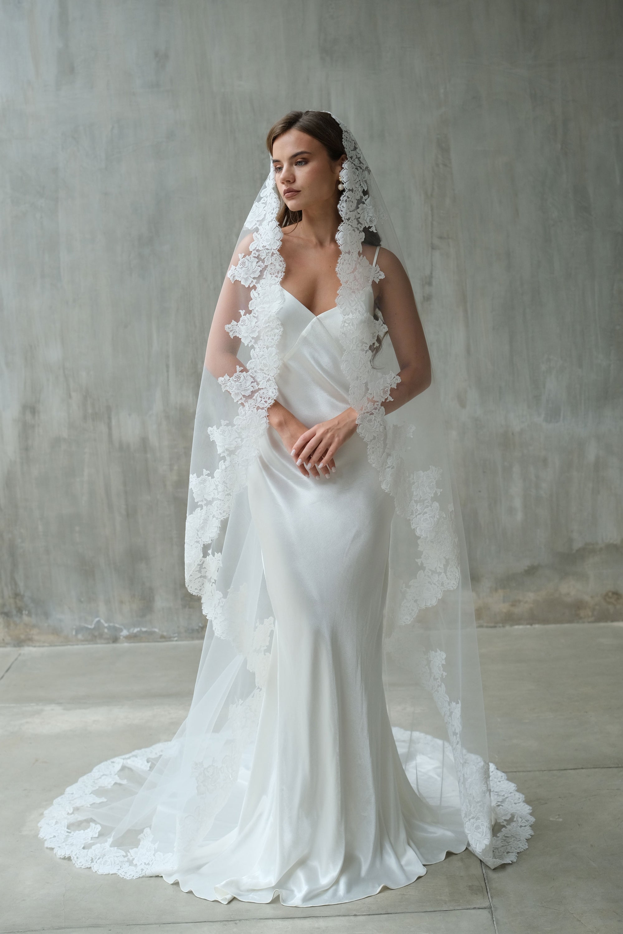 Front-facing shot of model wearing long, lace-edged mantilla wedding veil