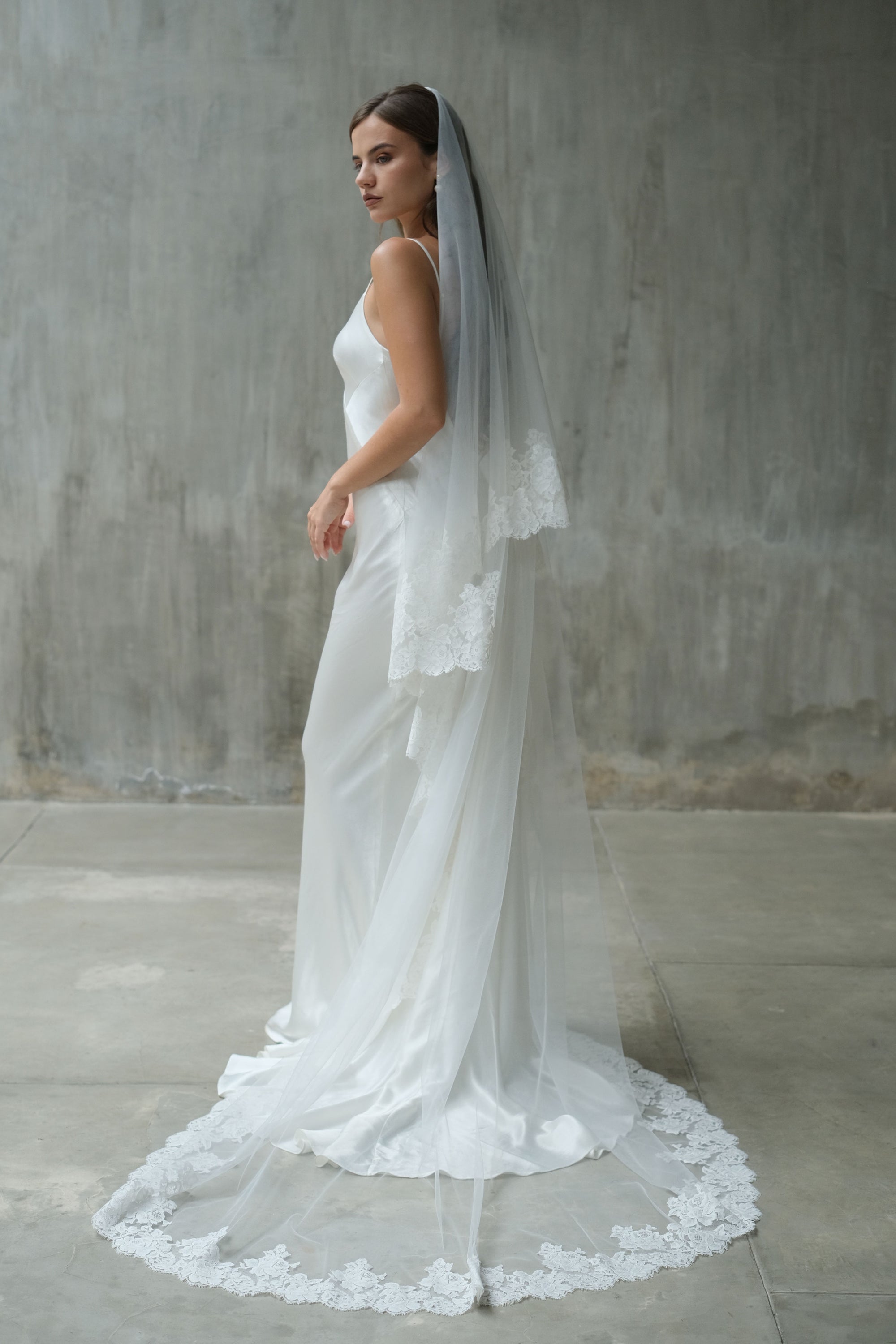 Bride turns in full length shot showing long romantic lace trimmed wedding veil with blusher off