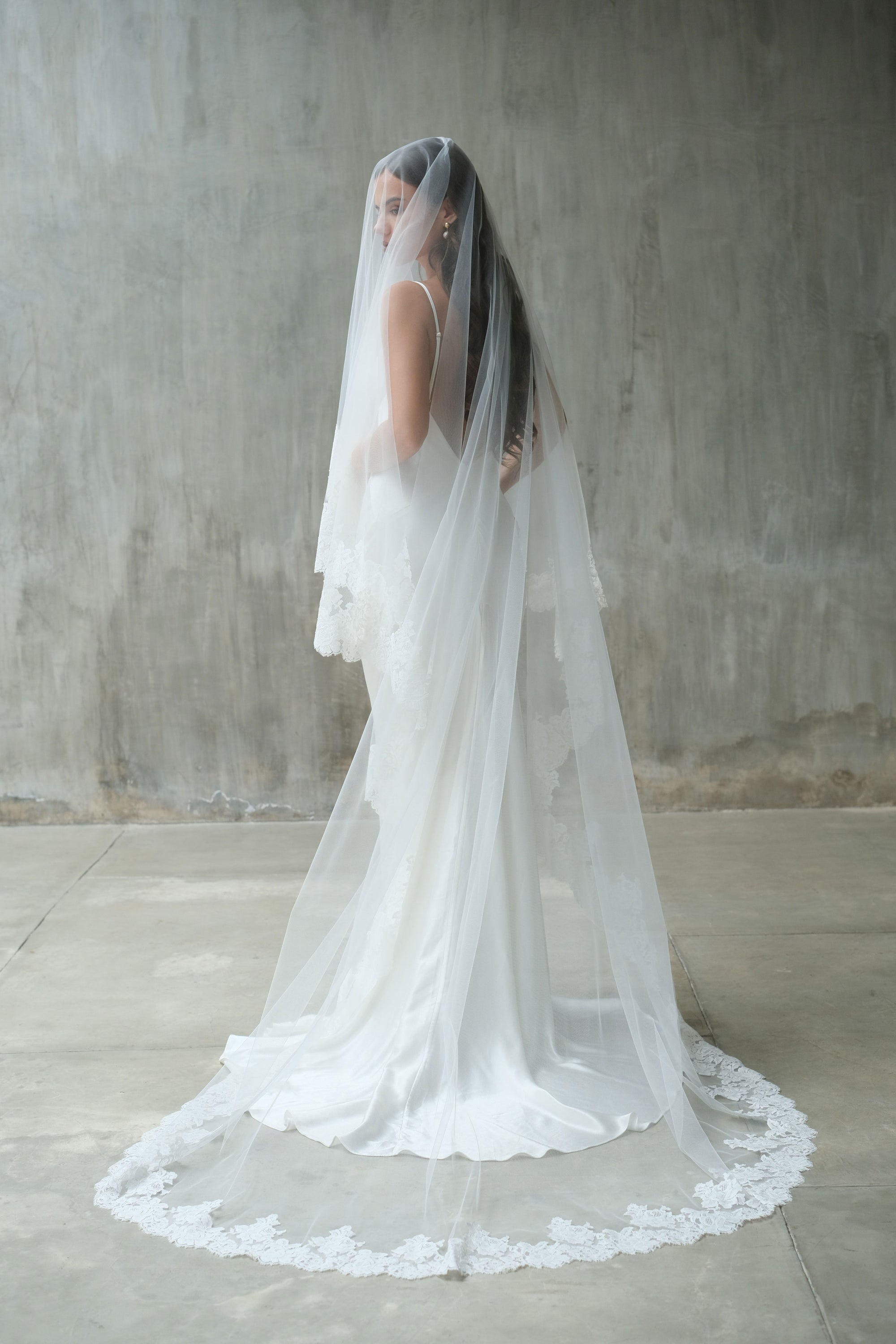 Full length shot of bride turning to show draping of lace trimmed two tier wedding veil shown with blusher down