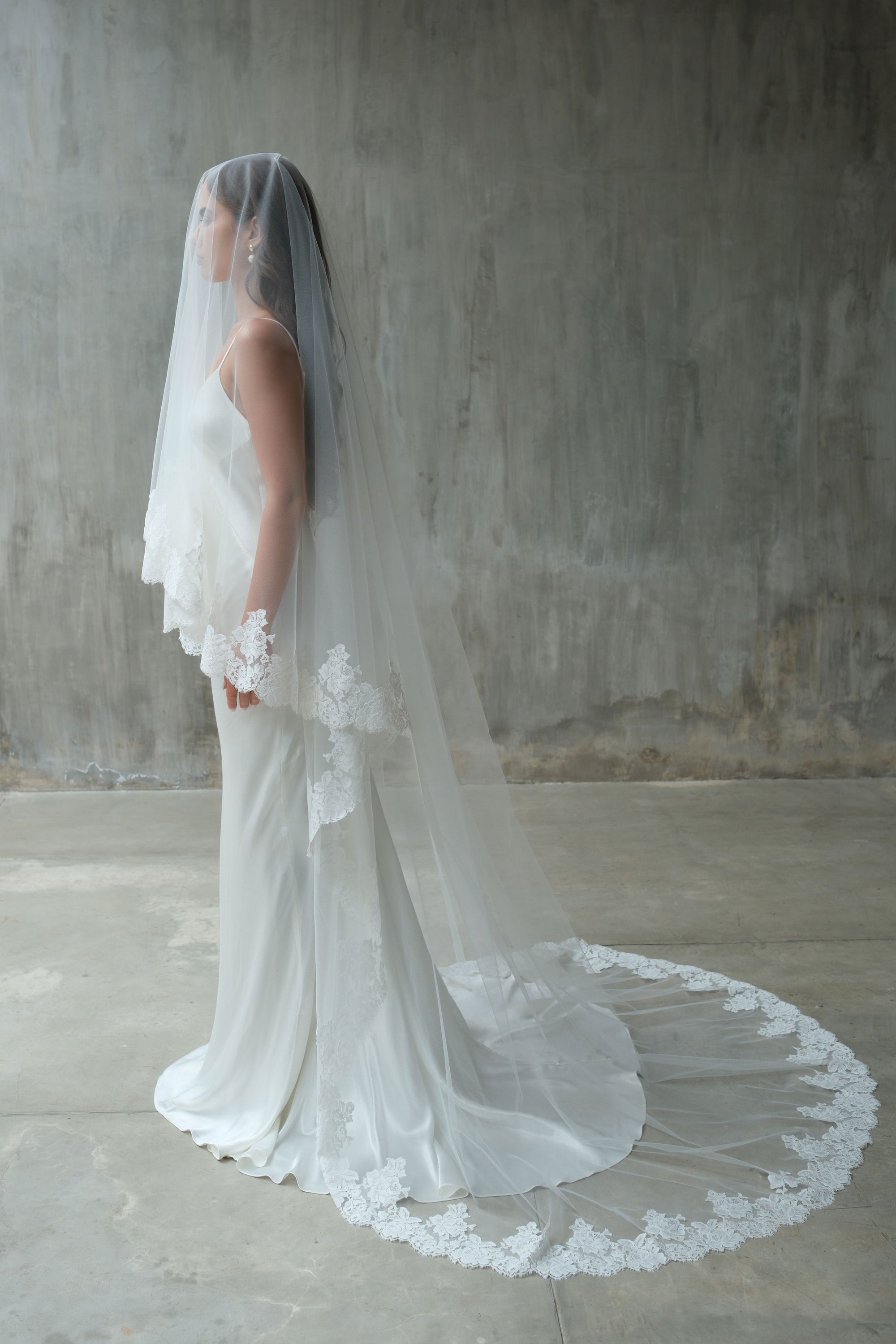 Full length side view of bride wearing chapel length wedding veil with lace edging and train fanned out to highlight romantic lace trim