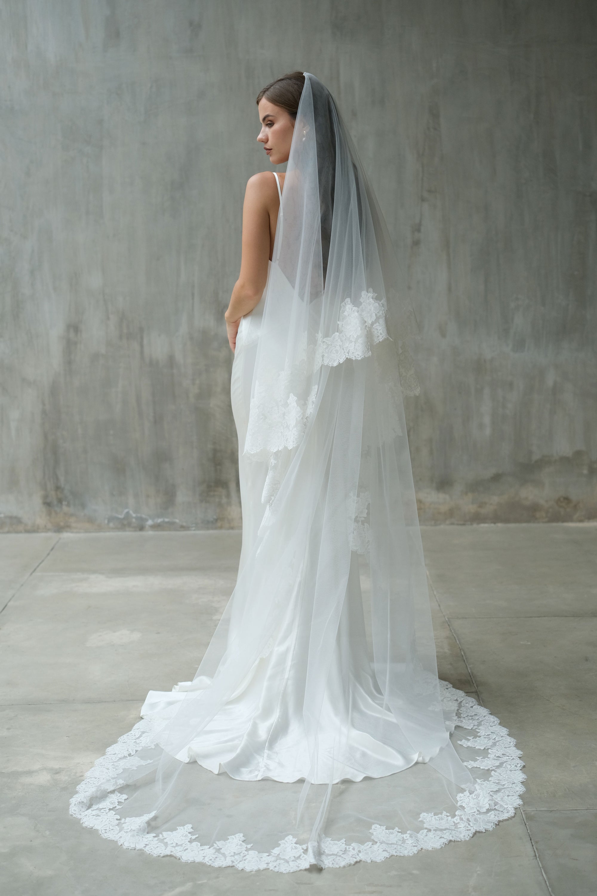 Full length back view of long two tier wedding veil trimmed with lace and showing blusher draped at the back
